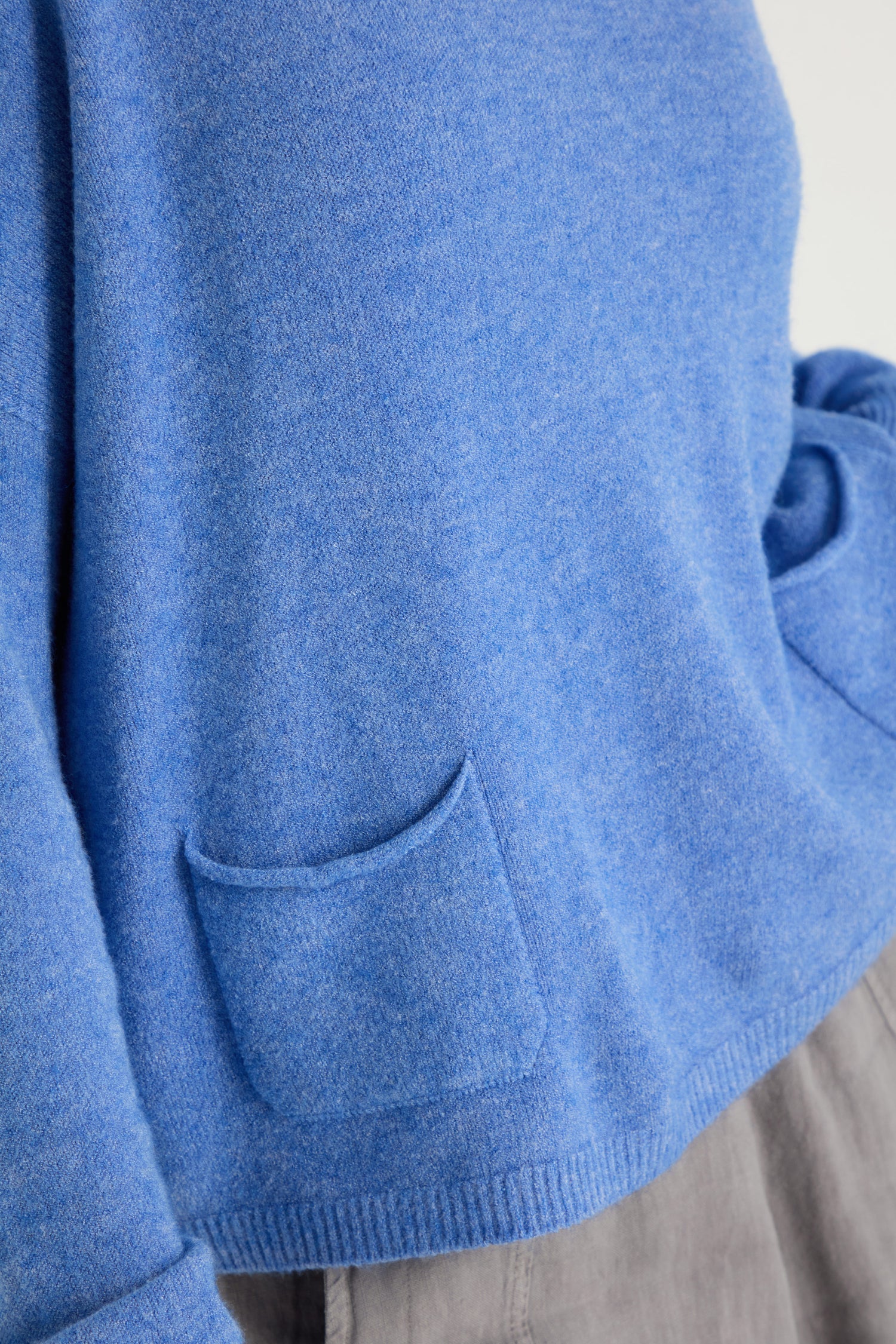 Someone wearing the Two Pocket Knit, a blue women's sweater featuring two small front pockets, paired with gray pants—ideal for everyday layering.