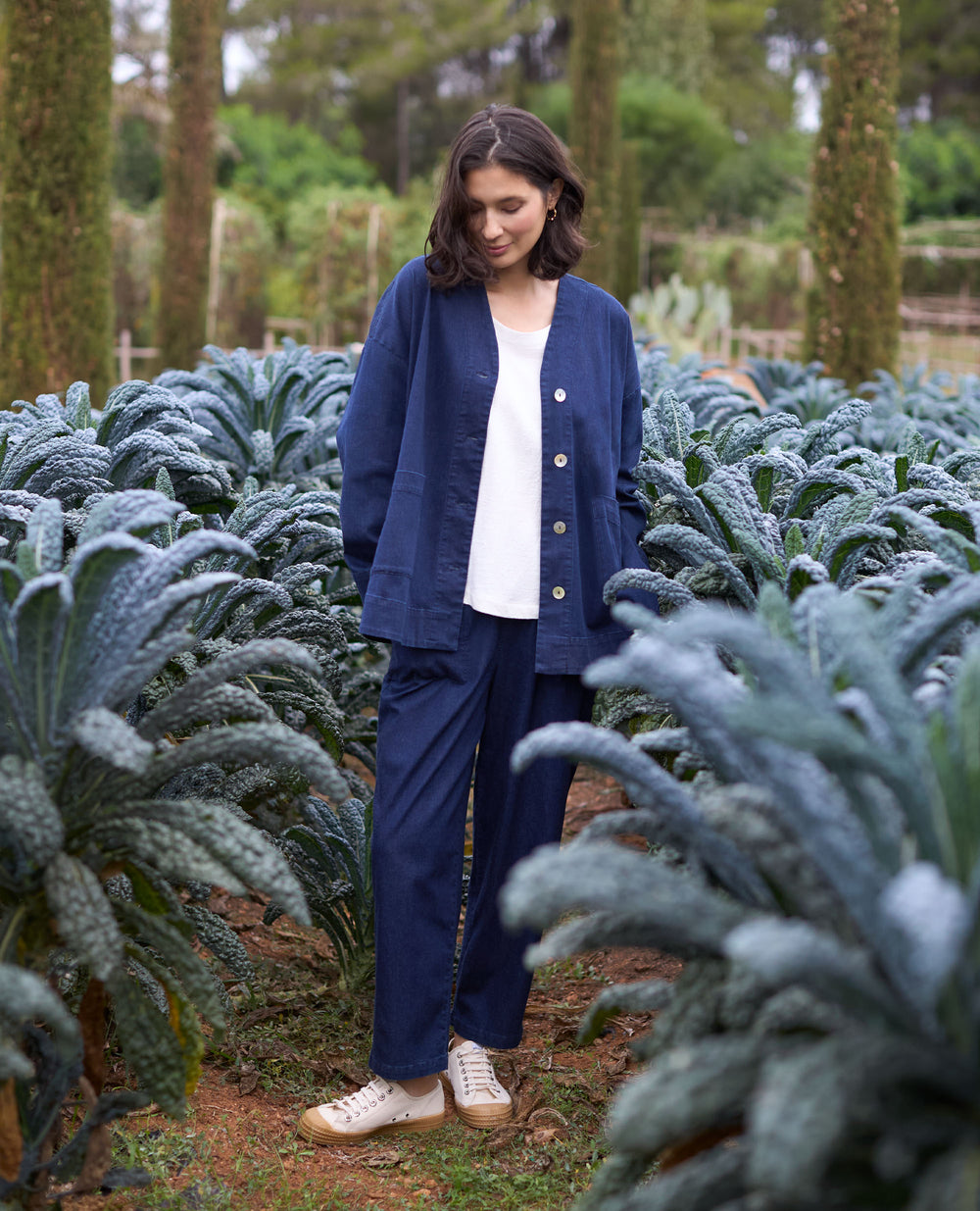 A woman in blue outfit stands in a kale field with vibrant greenery surrounding her.