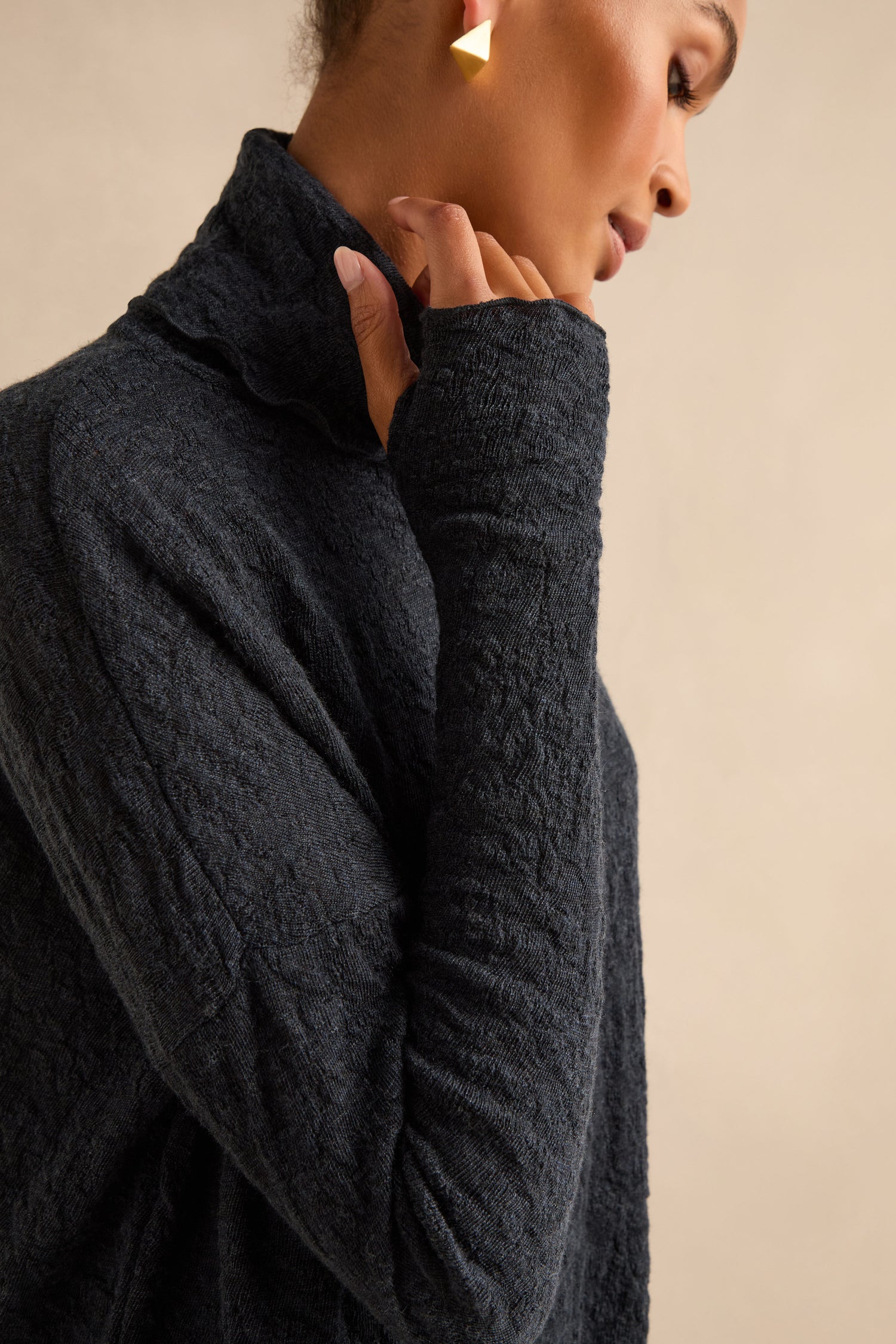 A person wearing the Navy Textured Merino Roll Neck Top poses with a hand near their chin against a neutral background.