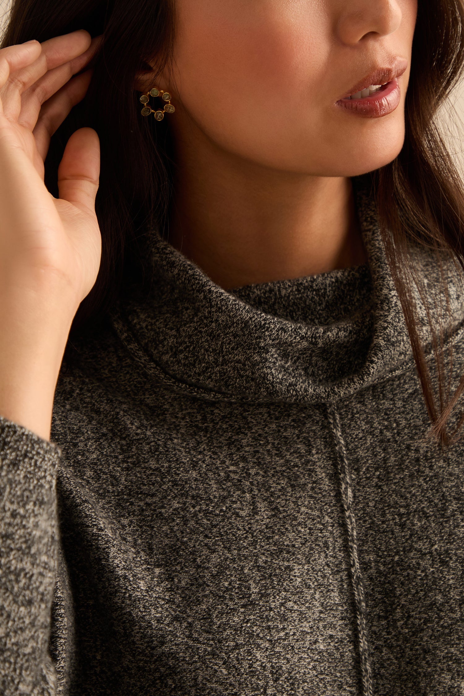 Woman wearing a black and white merino wool cowl neck jumper and gold floral earrings, shown from the shoulders up with her hand near her ear.