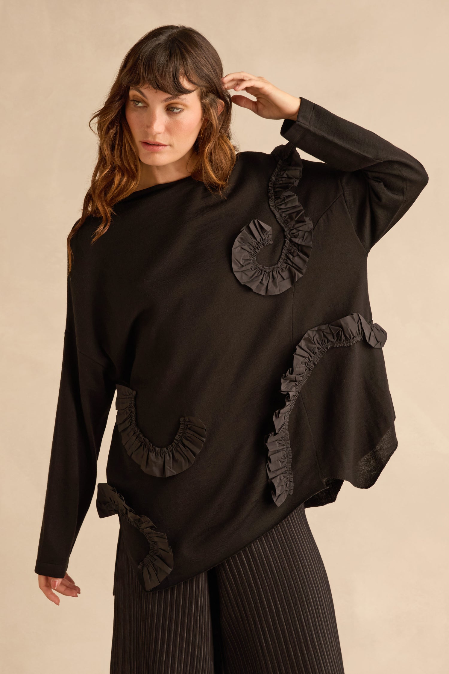 A woman wears a black Taffeta Detail Knit Top featuring relaxed knit fabric decorated with swirling taffeta ruffle appliqué.