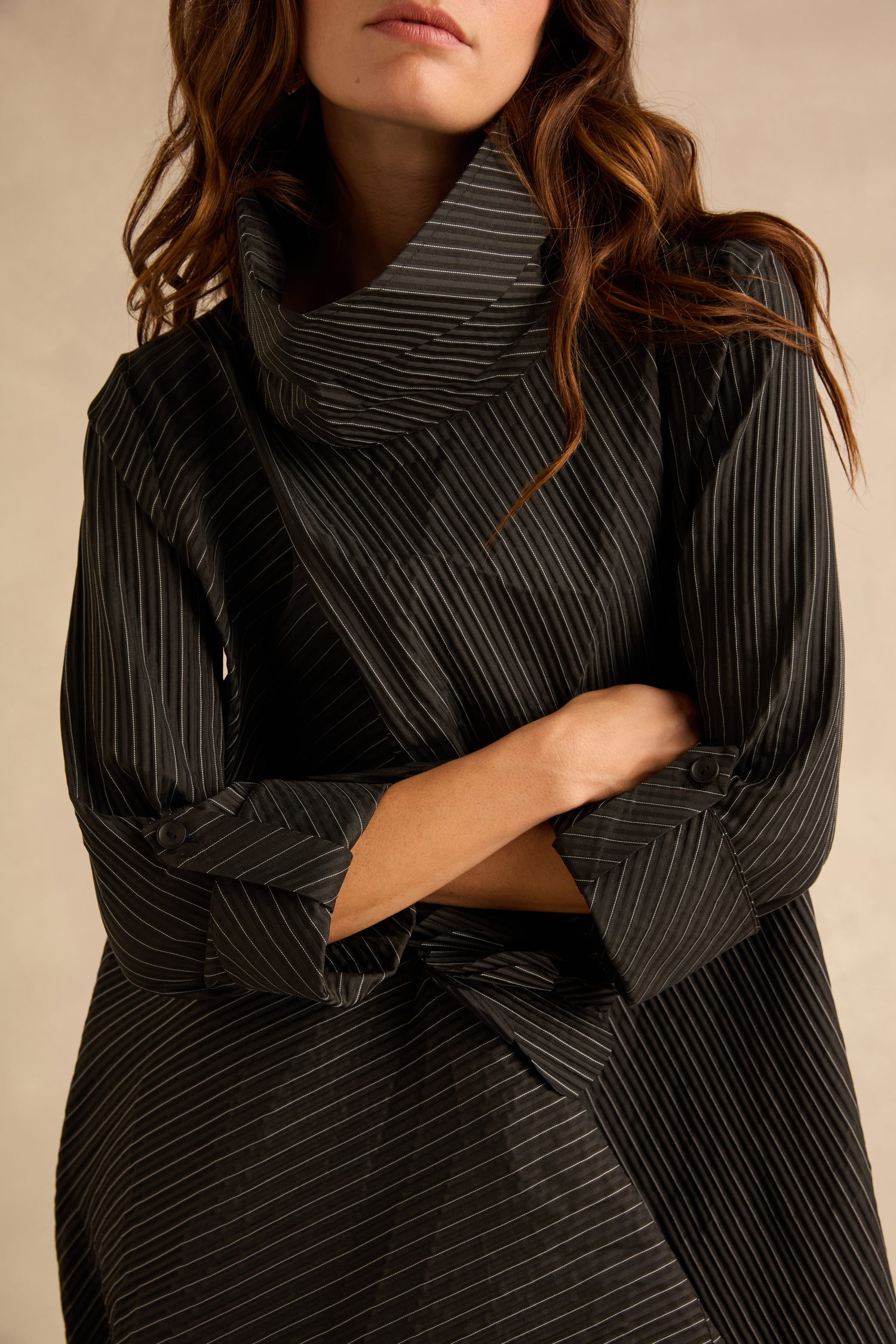 A Pin Stripe Flower Detail Dress in charcoal grey pinstripe with a pleated texture, high cowl neckline, cuffed sleeves, and a bubble hem.