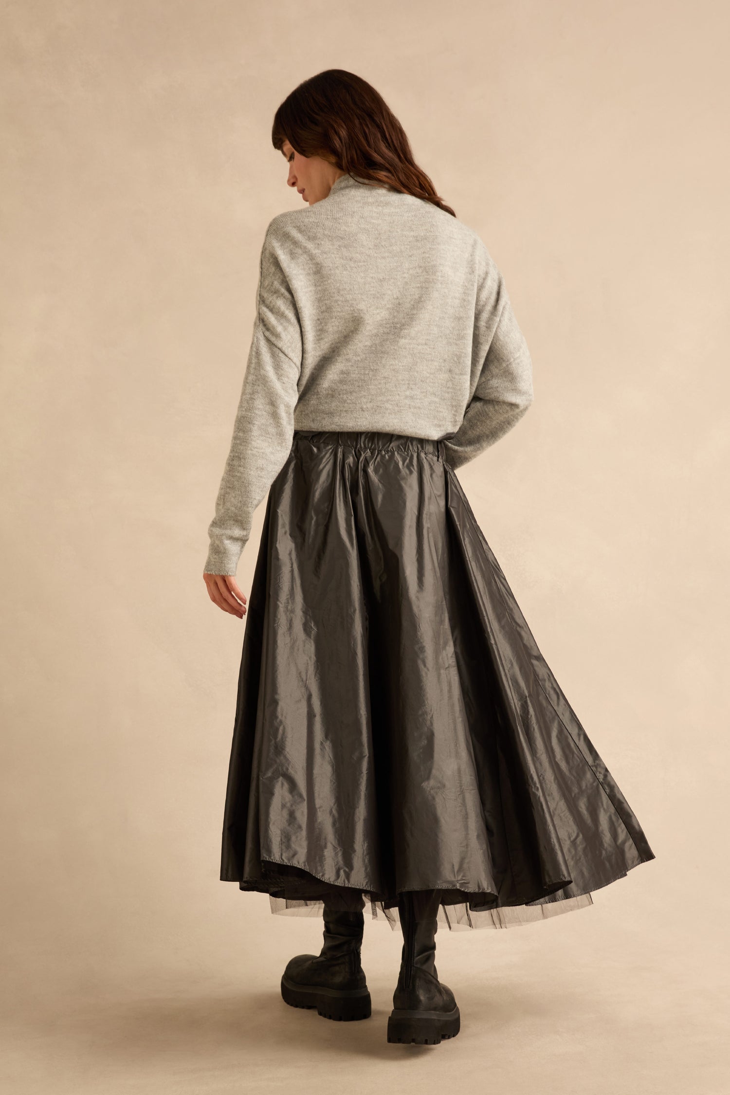 A person wearing a grey sweater and a metallic grey Flower Detail Taffeta Skirt with floral accents, paired with black boots.