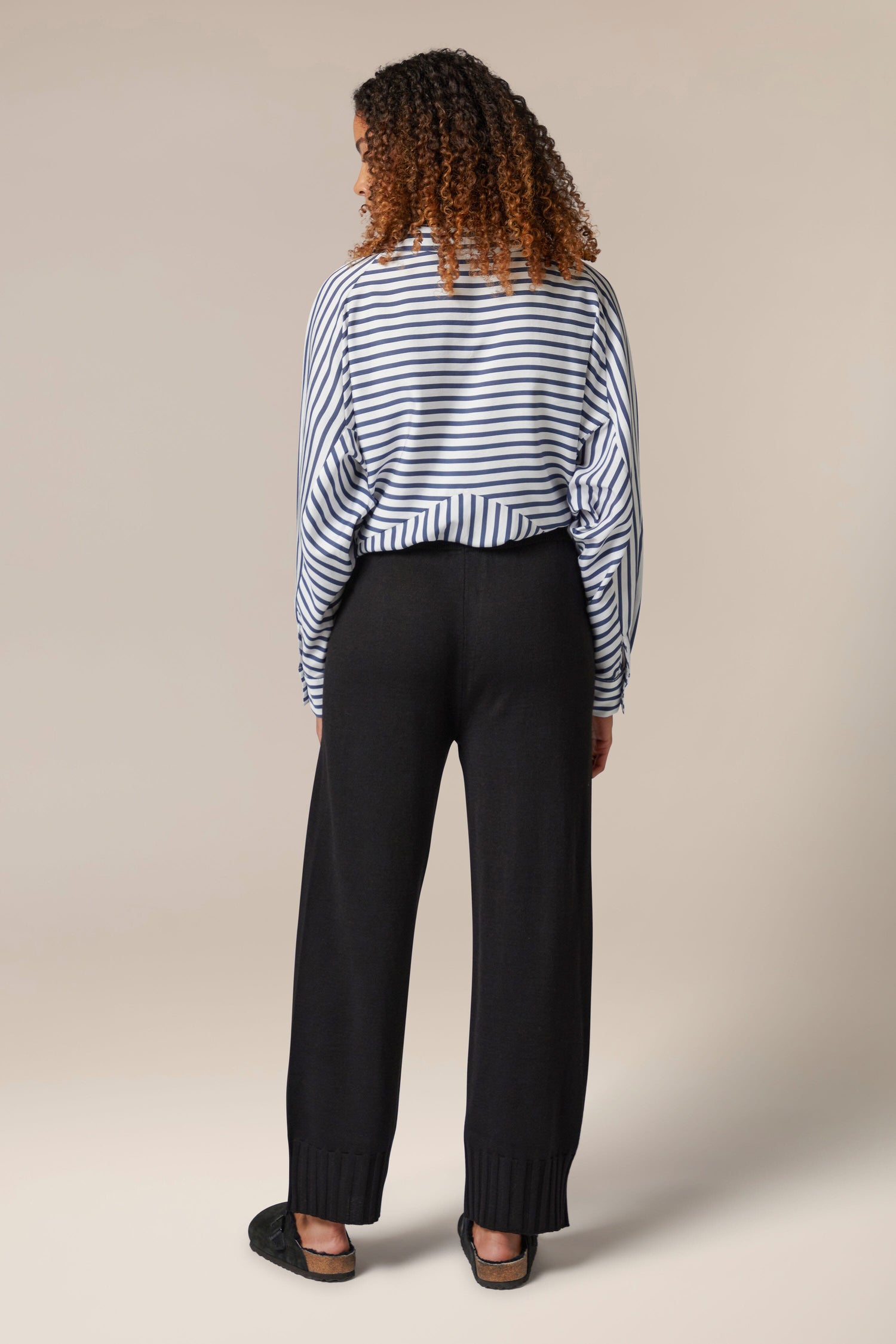 The back view of a woman wearing Rib Hem Knitted Trousers with a striped shirt.