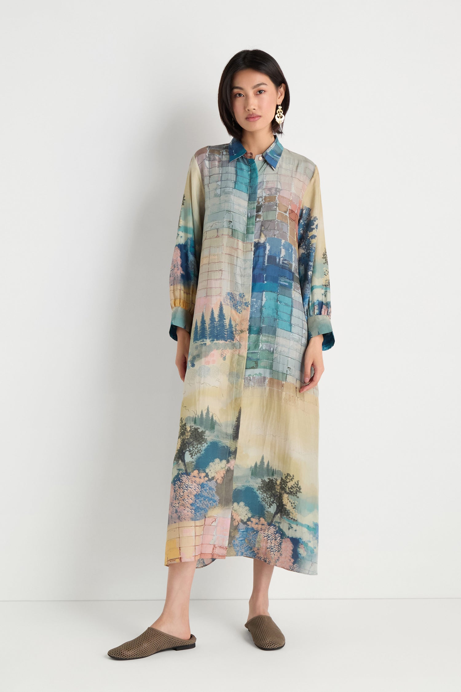 A woman wears the Horizon Silk Shirt Dress, featuring a scenic horizon print, styled with brown slip-on shoes and set against a plain white background.