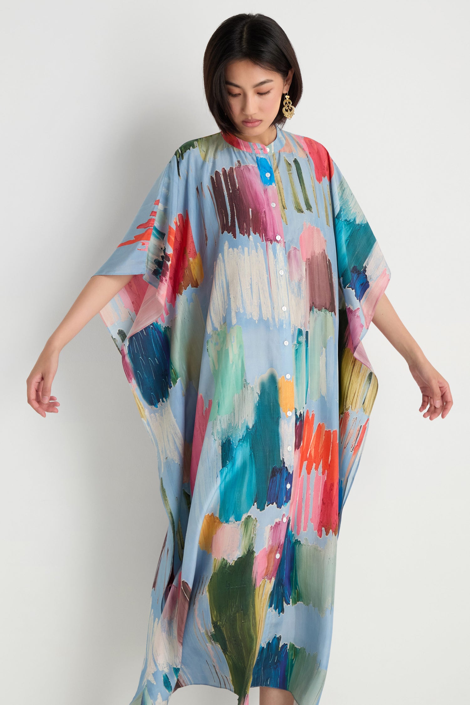 A woman models the Breezy Strokes Silk Shirt Dress, featuring a loose fit and colorful brushstroke print, set against a plain white background.