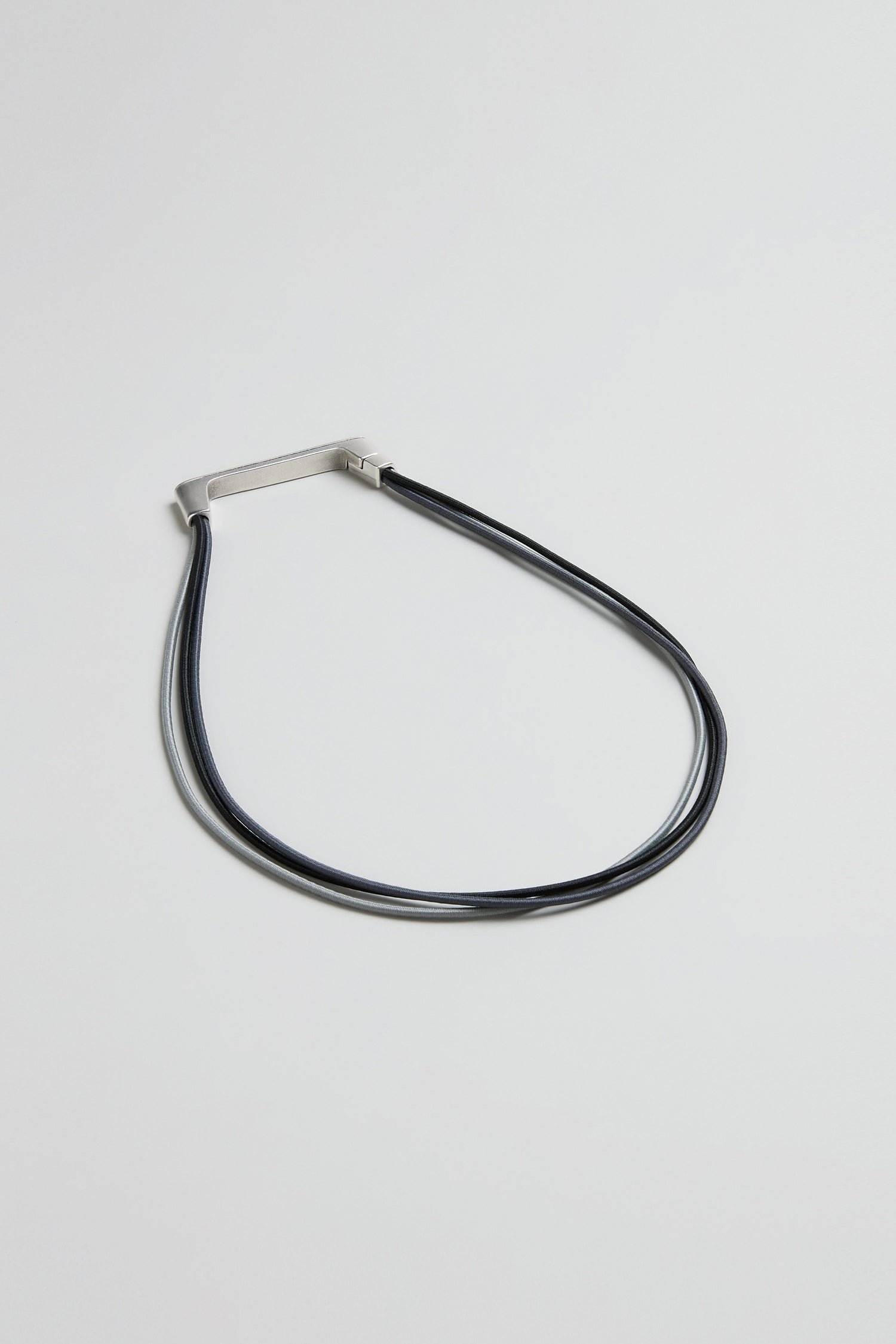 The Versatile Triple Cord Bracelet by Christina Brampti, shown against a plain light grey background, features a minimalist design with a rectangular silver accent on triple black cords.