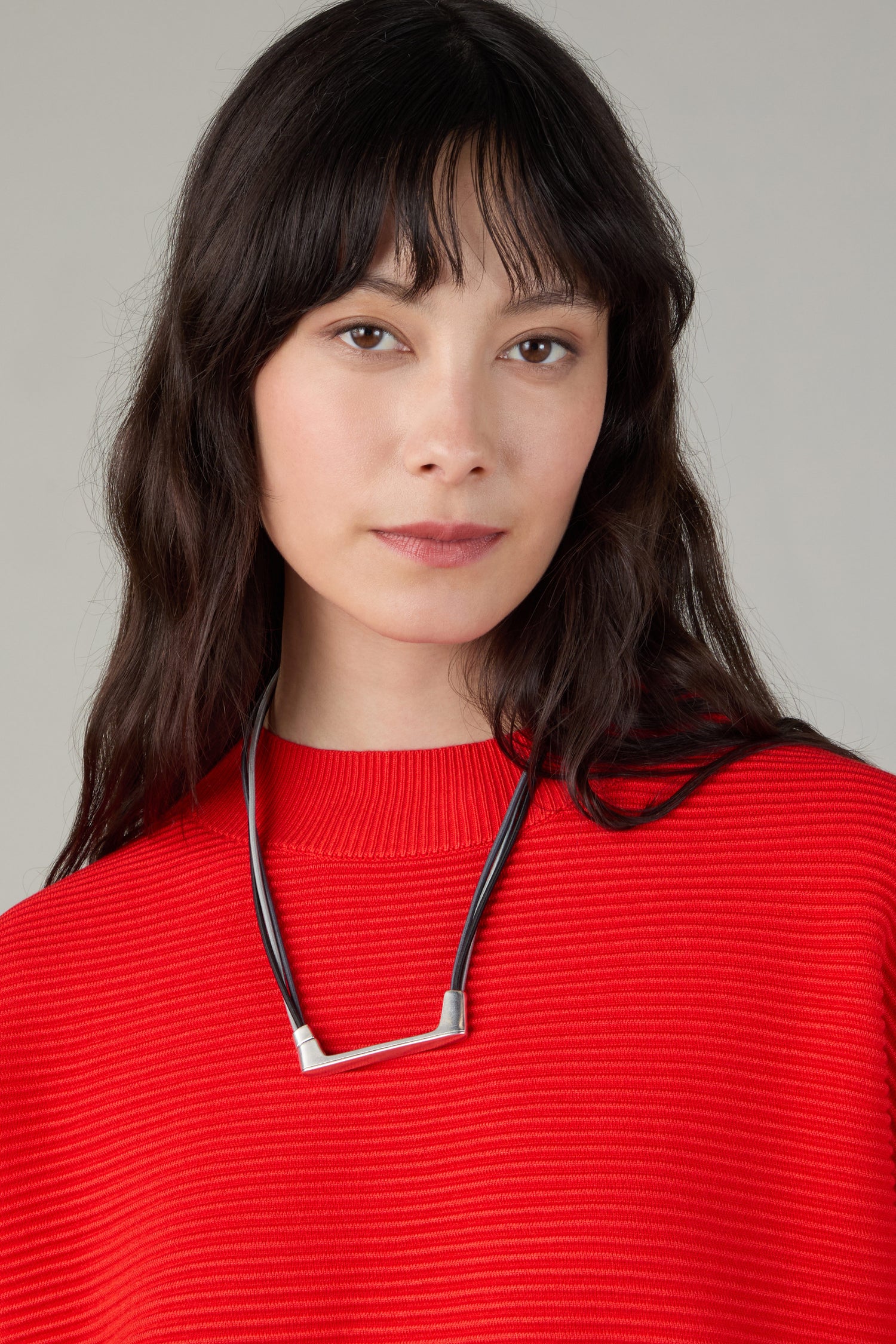Woman with long dark hair wearing a red textured sweater and the Versatile Triple Cord Bracelet, looking at the camera with a neutral expression.