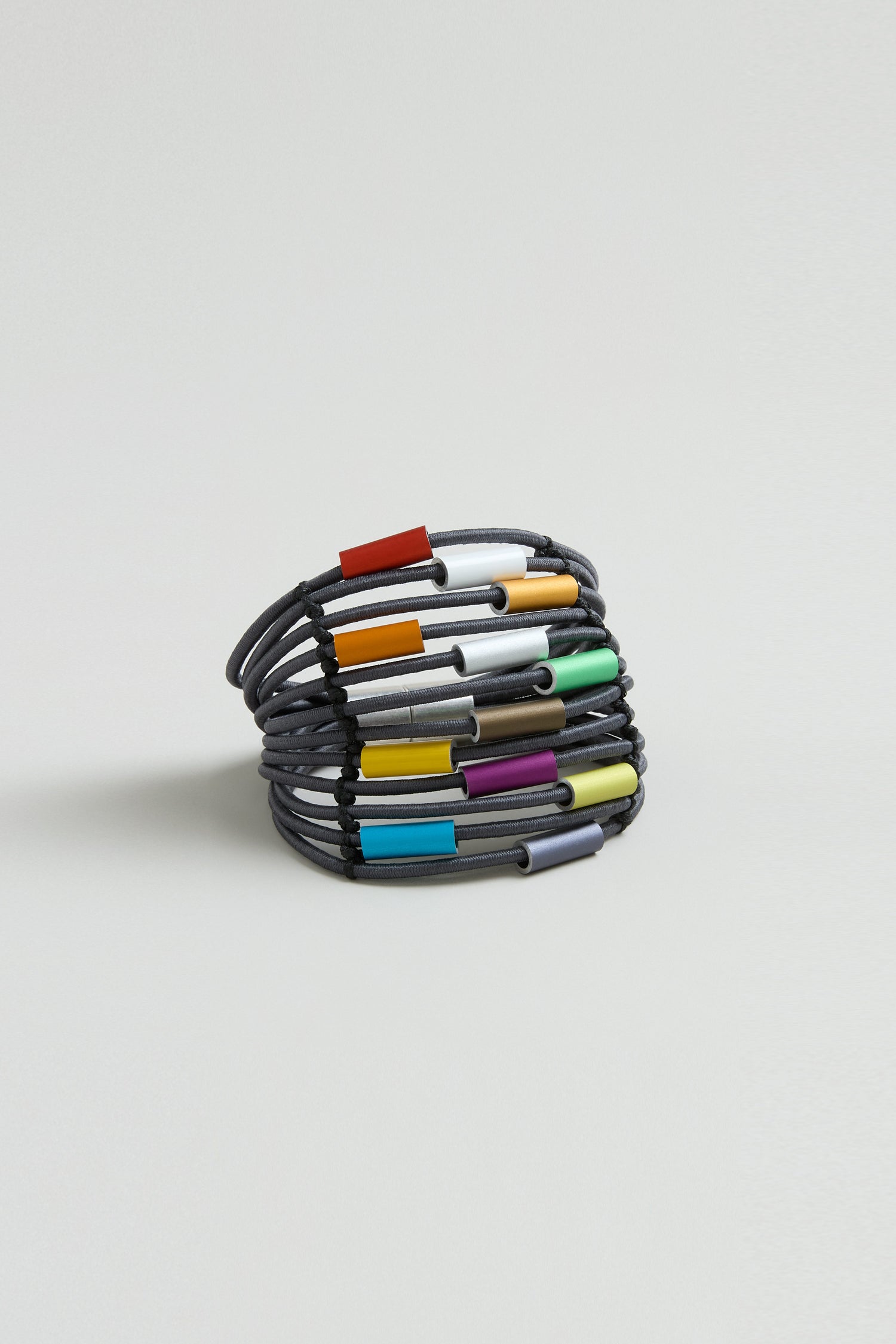The Colour Pop Cylinders Bracelet by Christina Brampti features a coiled black design with multicolored rectangular beads, presented on a plain light background—a bold statement of contemporary jewelry.