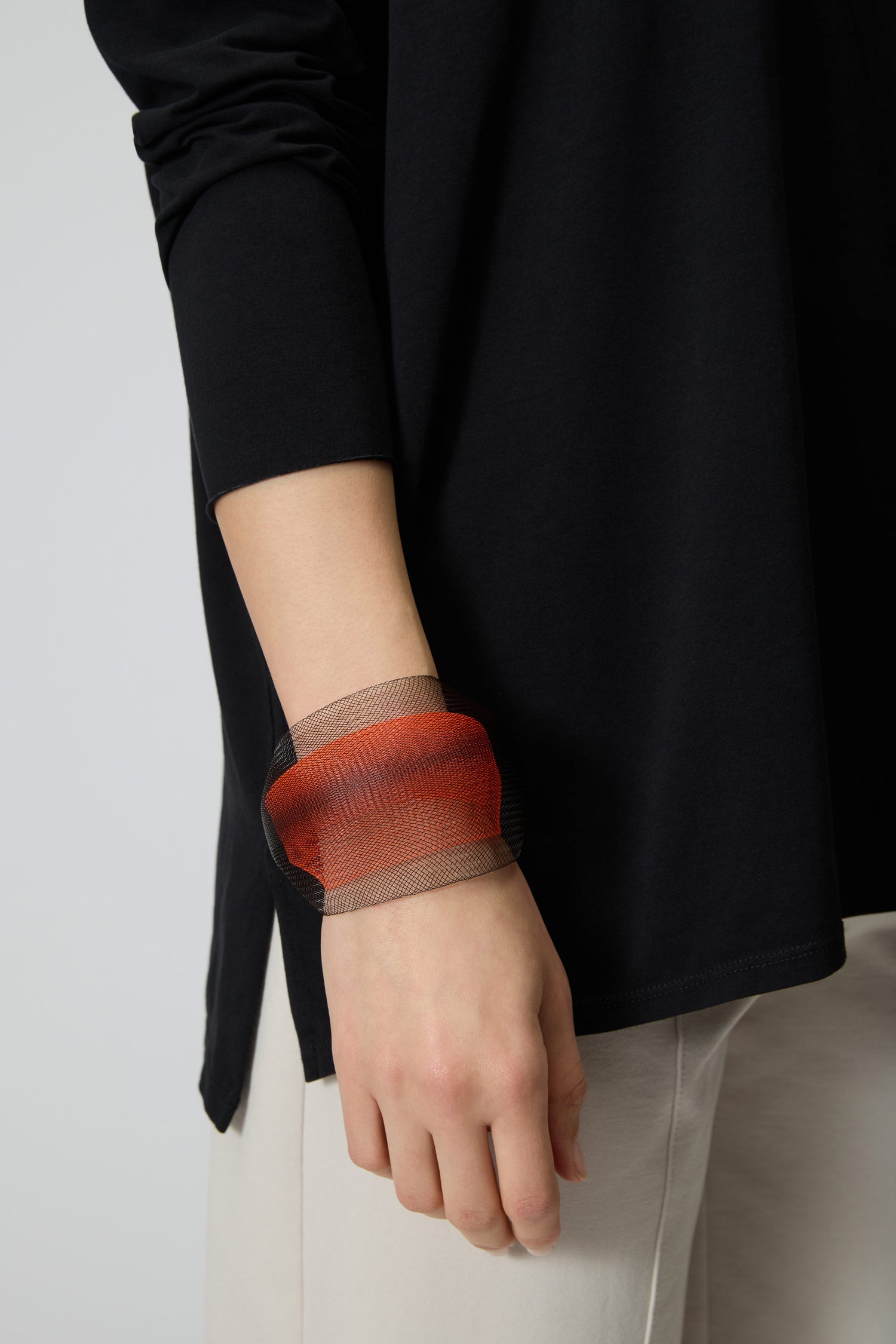 A person wearing a long-sleeved black top and light-colored pants with the Orange Statement Mesh Bracelet on their wrist.