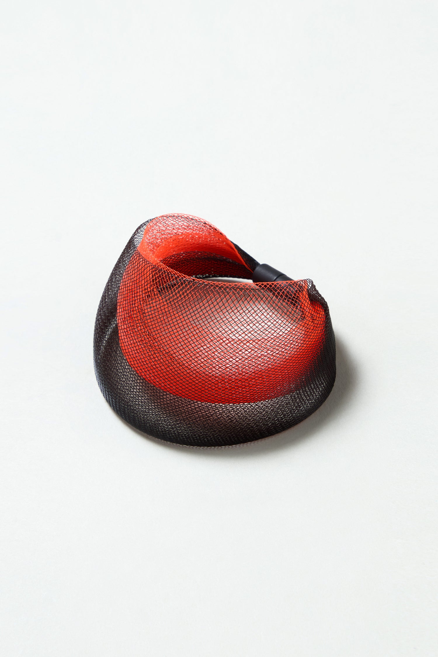 An orange statement mesh bracelet with a round, sculptural design and a shallow, bowl-like shape rests on a plain light surface.