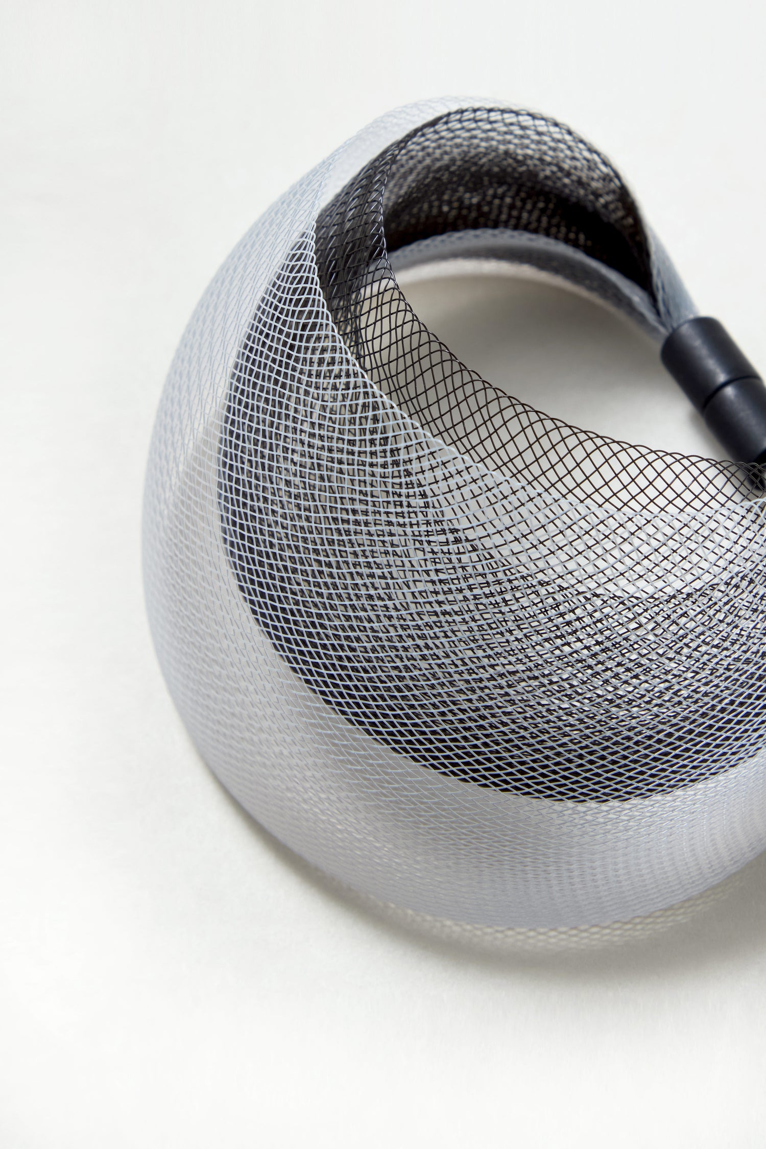 A close-up of the Silver Statement Mesh Bracelet reveals its coiled black and white mesh, evoking intricate, sculptural patterns reminiscent of minimalist jewelry, all set against a plain white background.