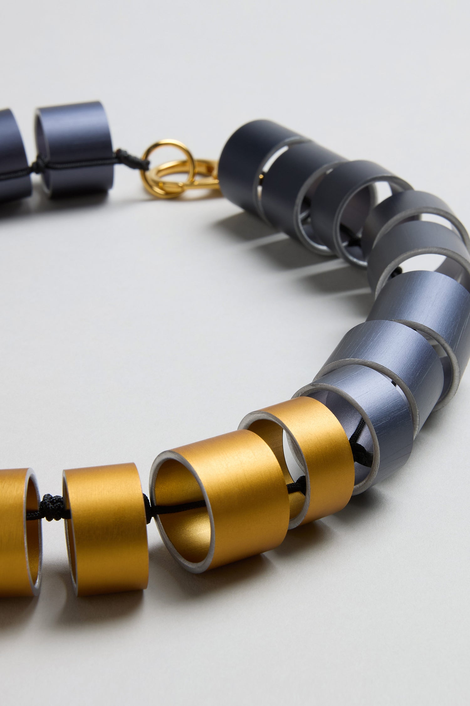 A close-up of the Geometric Cylinders Necklace by Christina Brampti, featuring alternating gold and silver cylindrical beads on a black cord with a gold clasp—a striking piece of statement jewellery.