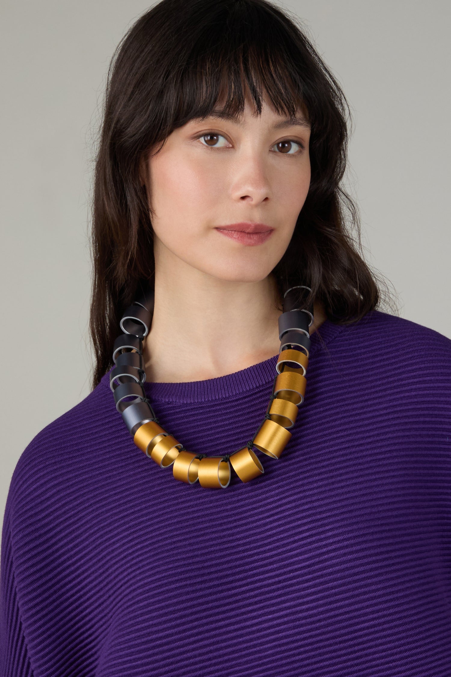 Woman with straight dark hair wears a textured purple top and the Geometric Cylinders Necklace by Christina Brampti, looking at the camera with a neutral expression.