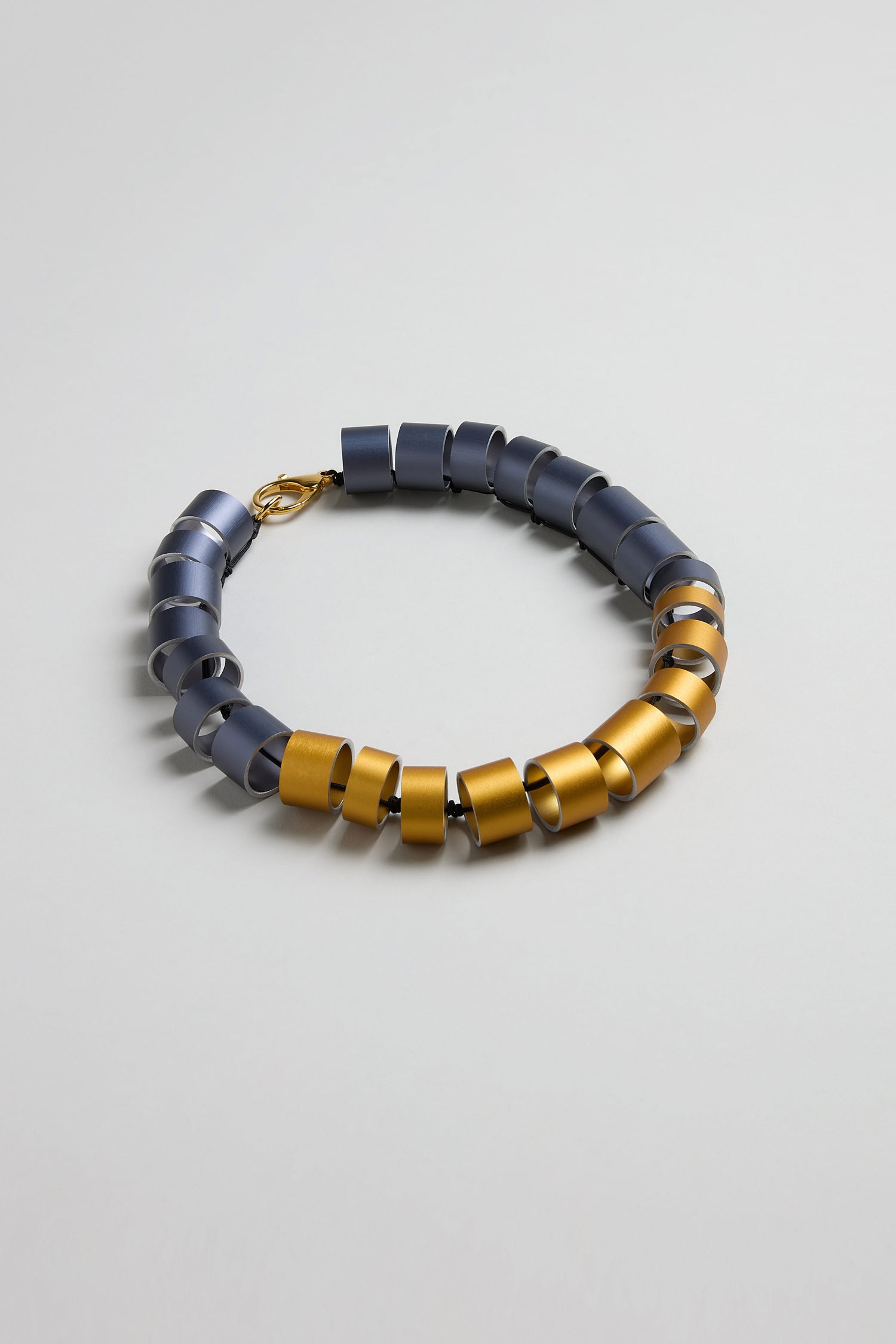 The Geometric Cylinders Necklace features alternating blue and gold metallic segments in a circular pattern with a gold clasp, showcasing Christina Brampti’s bold statement jewellery style.