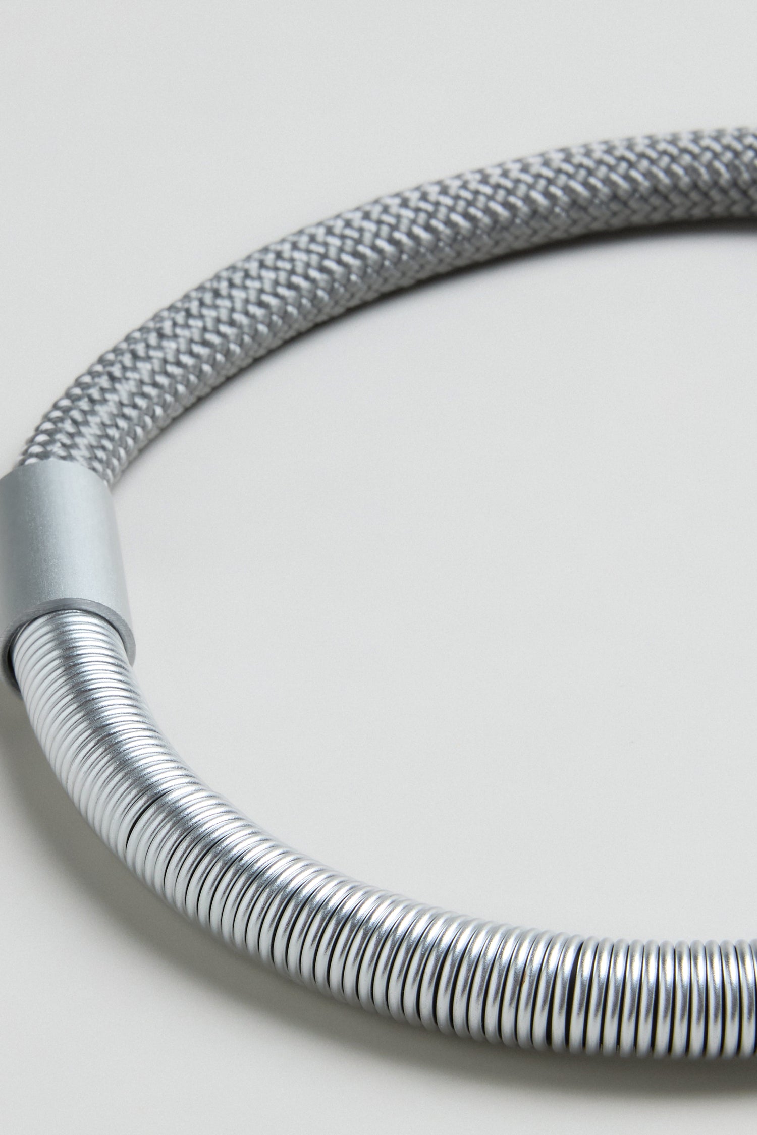 Close-up of the Flow Cord Necklace, featuring flexible coiled and braided silver sections, reminiscent of contemporary jewellery design, set against a plain light background.
