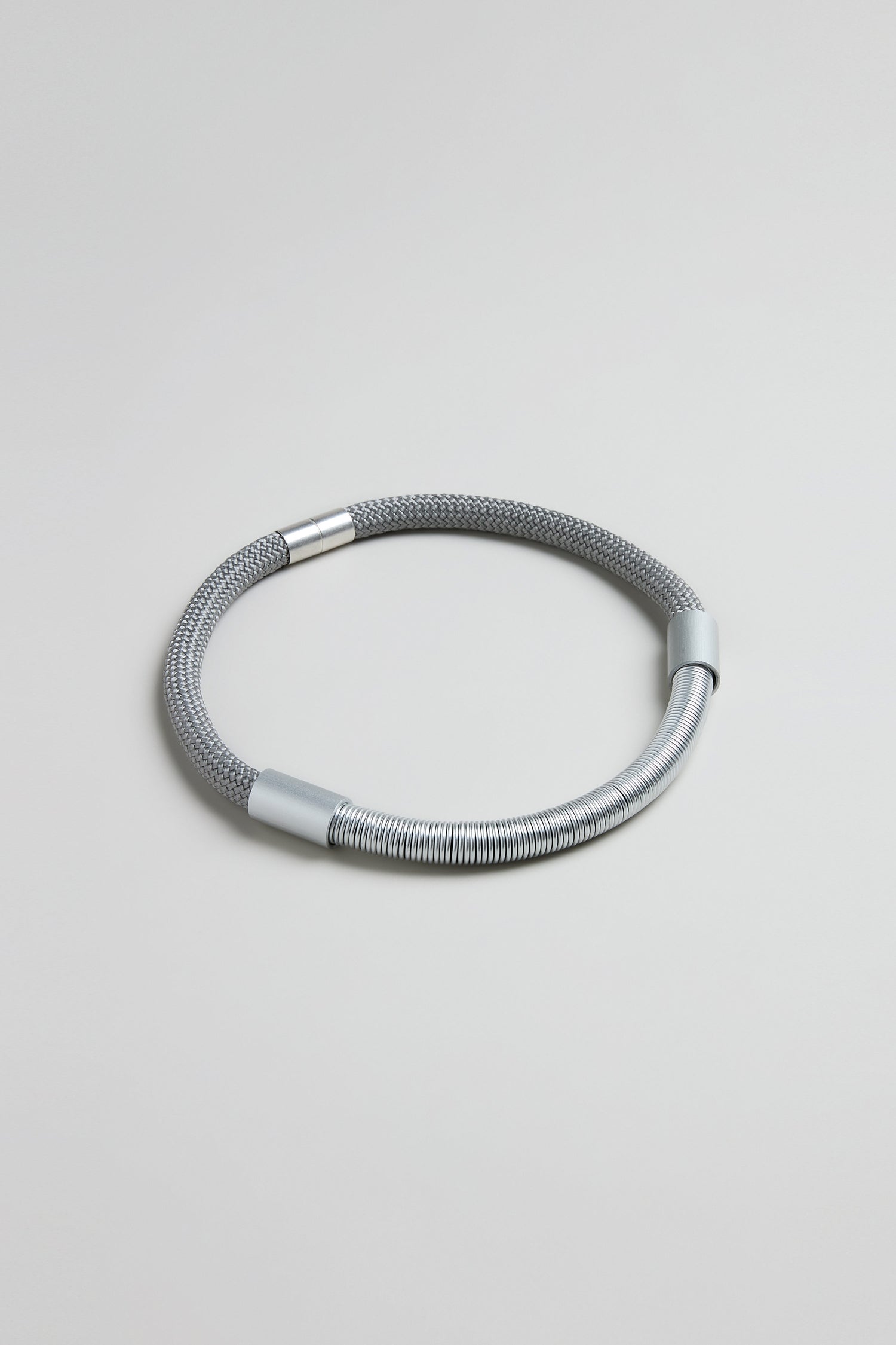The Flow Cord Necklace features a textured mesh cord with smooth metal accents, embodying sleek contemporary style. Shown against a plain light gray background.