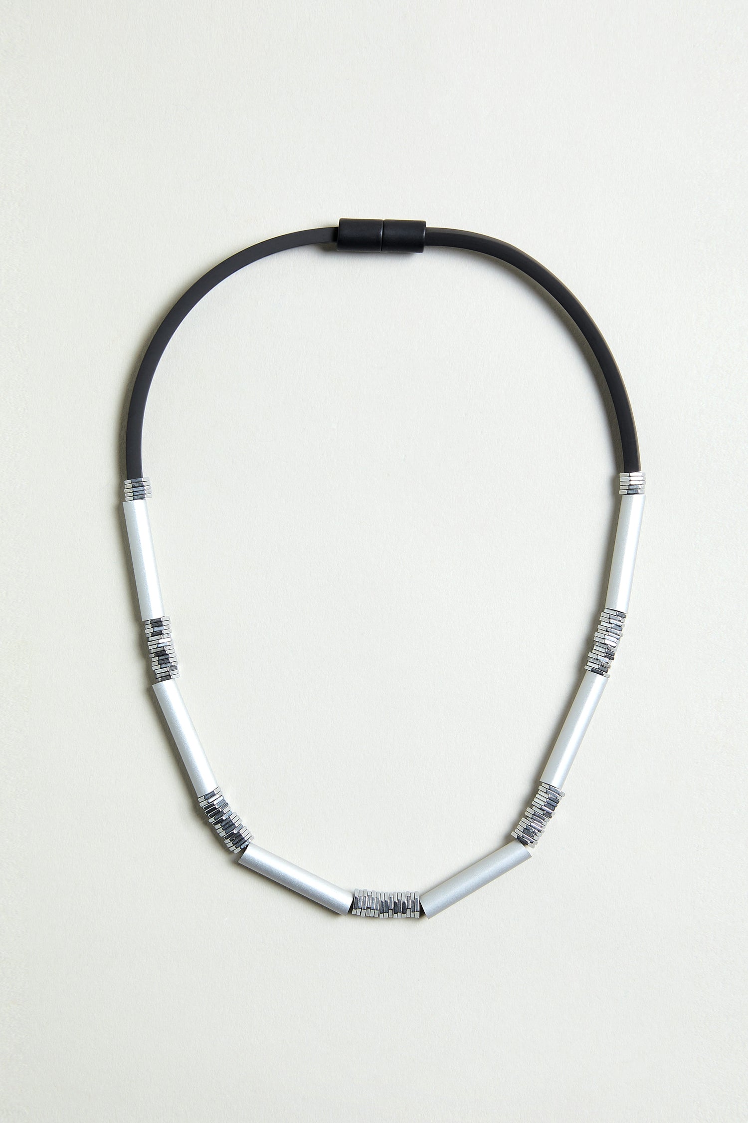 The Silver Aluminium Hematite Necklace is a contemporary design by Christina Brampti, featuring black rubber and six silver anodised aluminium segments wrapped in thin wire, shown on a plain light background.