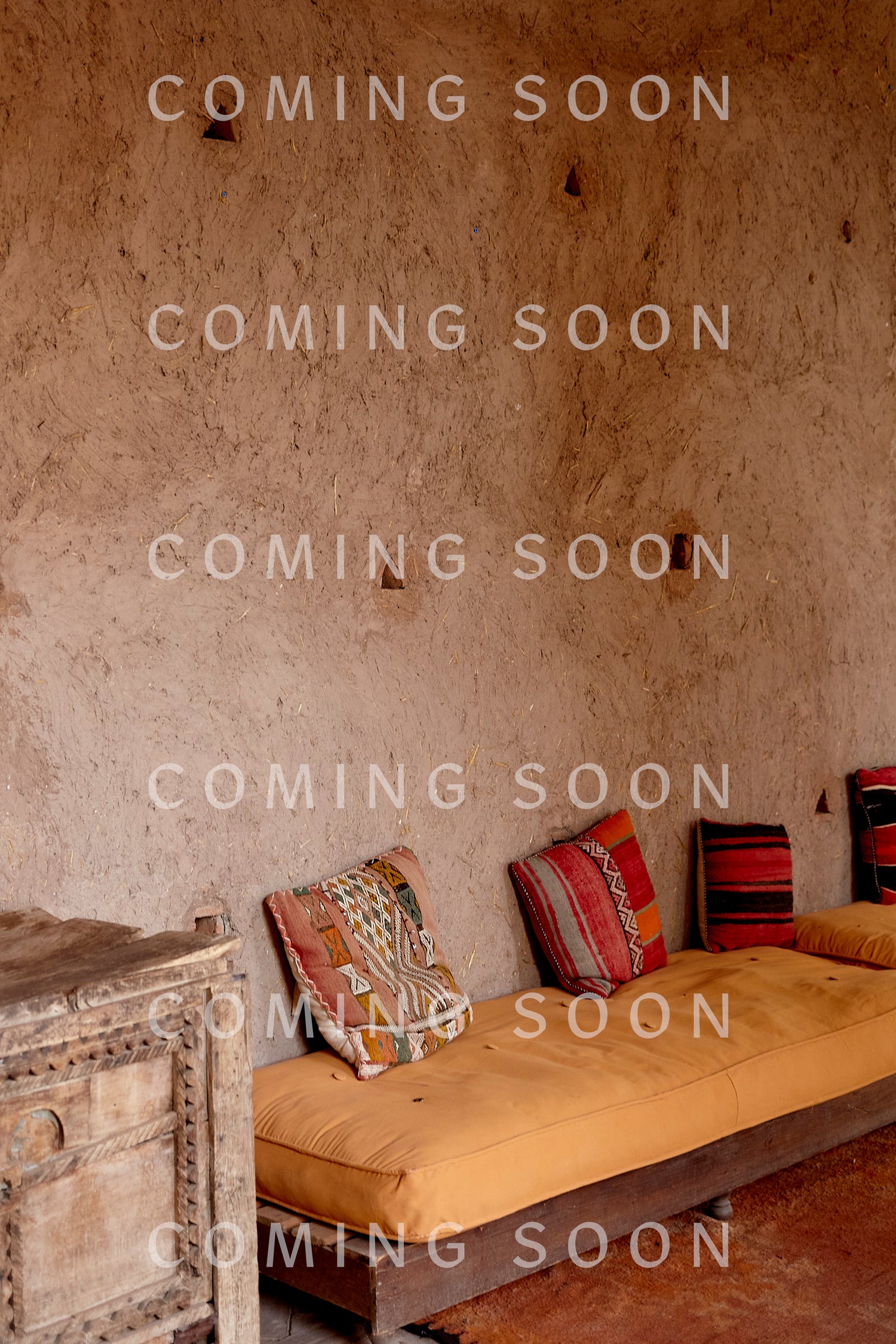 A rustic room with a textured plaster wall, wooden cabinet, and low seating with patterned cushions—perfect for lounging in the Cotton Jersey Boxy Pocket Top.