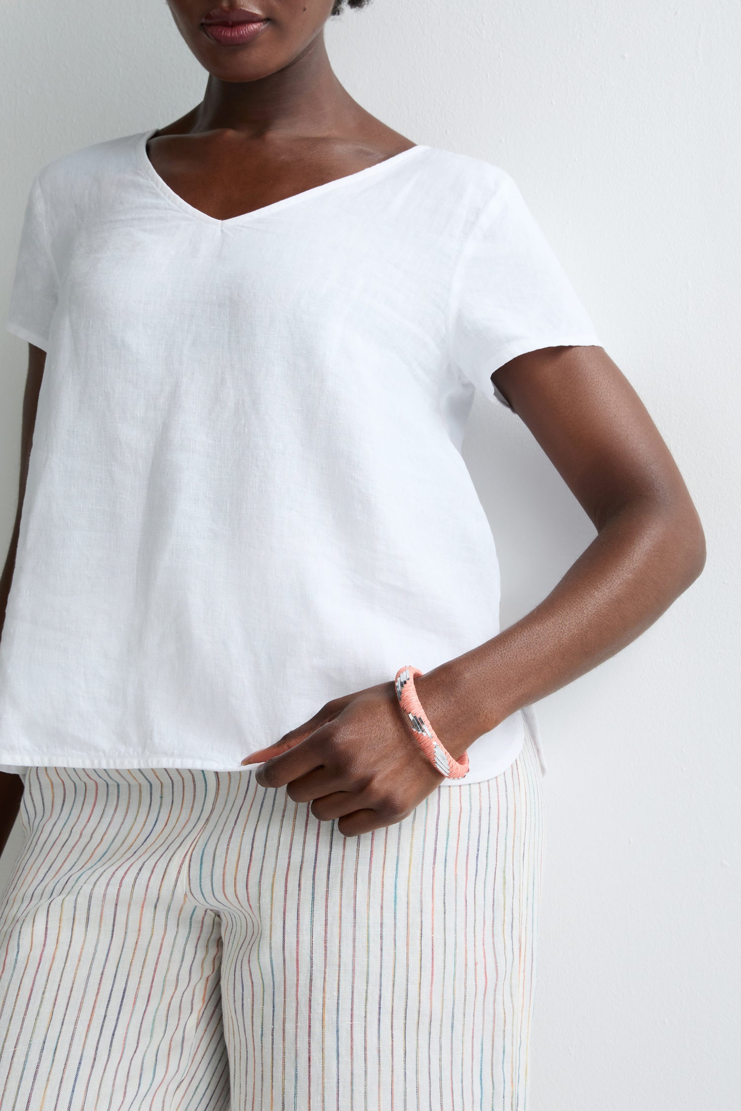 A person wearing a white short-sleeve V-neck top, striped pants, and the Handwoven Silver Chevron Bangle stands against a white background.
