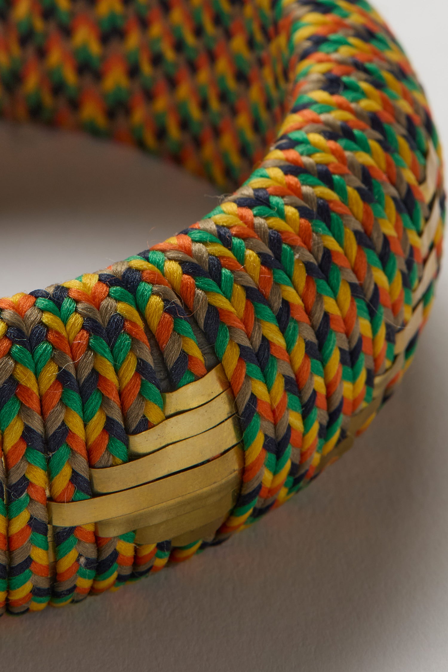Close-up of the Handwoven Multicoloured Bangle, featuring vibrant orange, yellow, green, and dark blue threads with light tan bands that highlight its heritage craftsmanship.