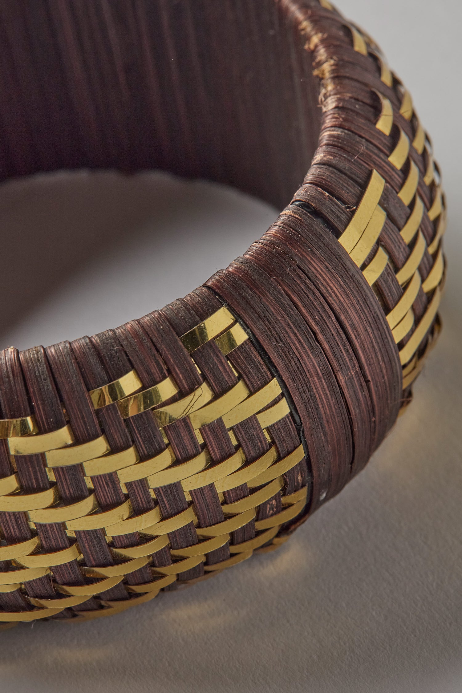 Close-up of the Handwoven Espresso Bangle, showcasing its dark brown material interlaced with shimmering golden threads in a delicate zigzag pattern.