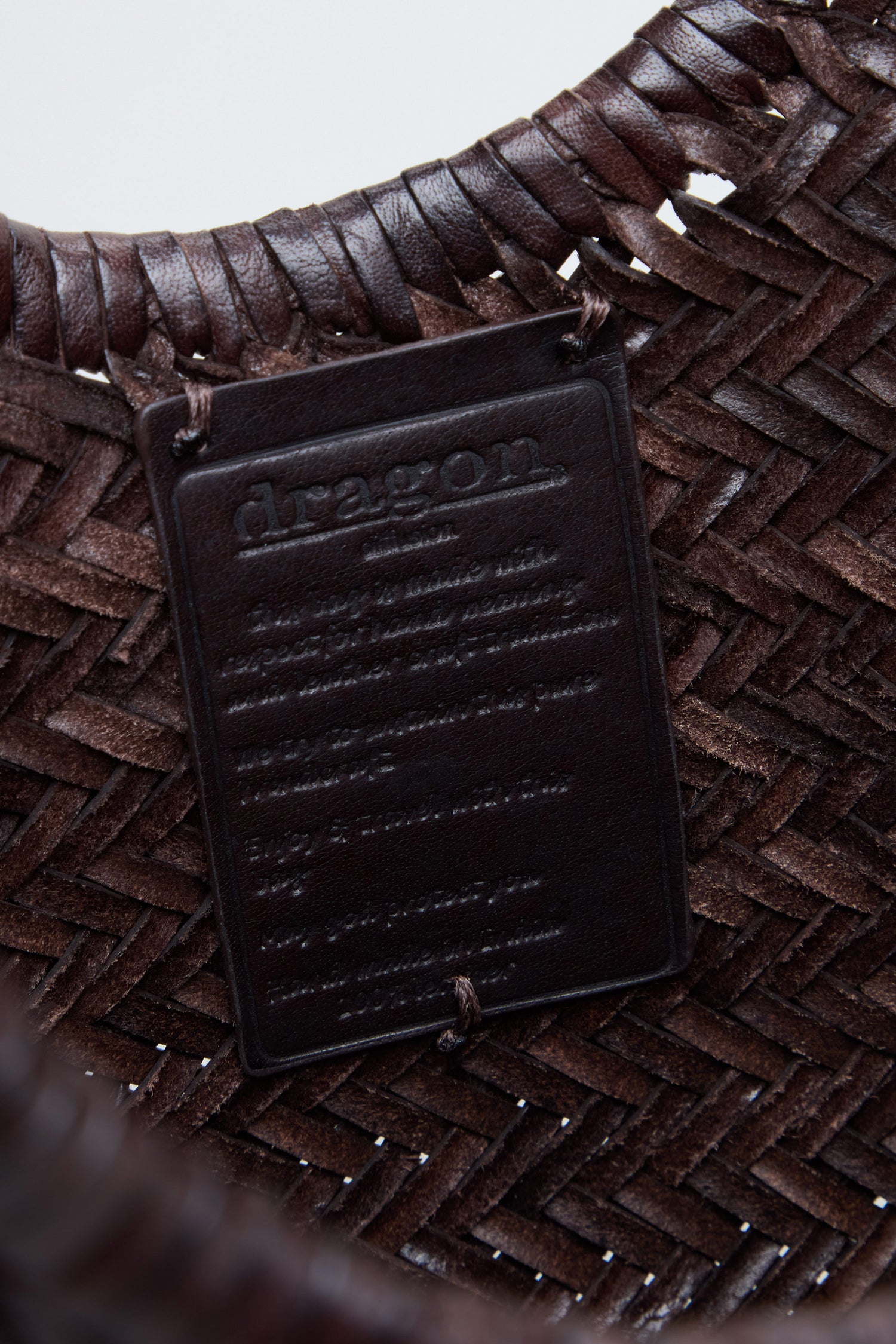 Close-up of the Nantucket Woven Dark Brown Leather Bag, featuring a handwoven design and a rectangular leather label embossed with "dragon" and additional text beneath, highlighting the signature craftsmanship of Dragon Diffusion.