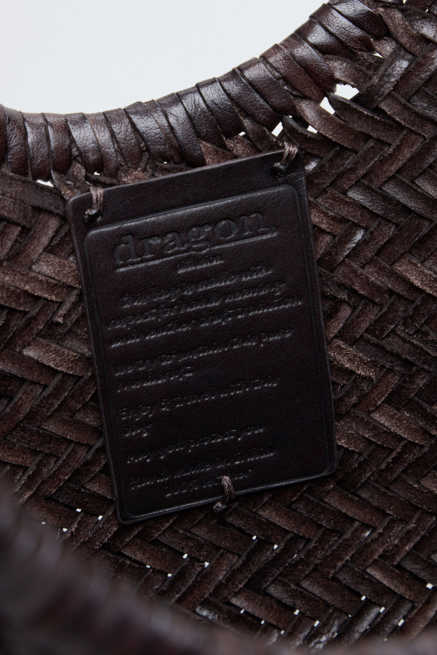 Close-up of the Nantucket Woven Dark Brown Leather Bag, featuring a leather label embossed with "dragon" and additional text beneath it, highlighting the artisanal craftsmanship of Dragon Diffusion.