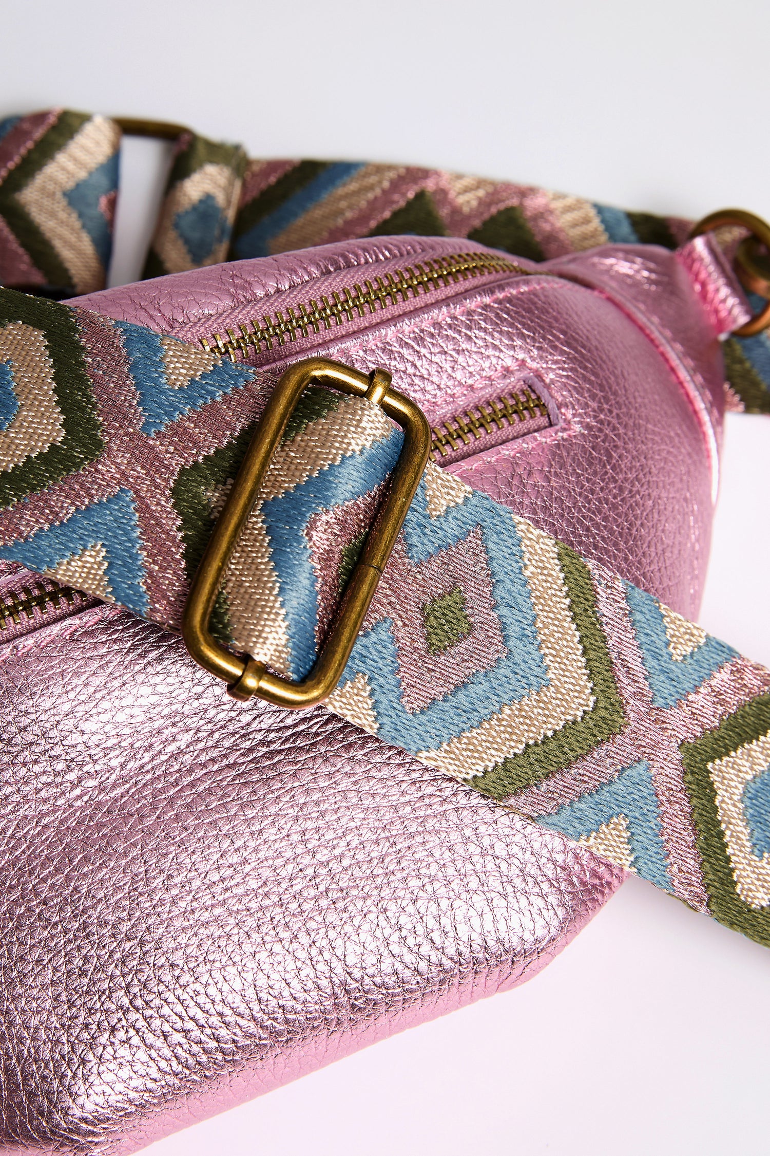 Close-up of the Metallic Leather Crossbody Bag by Doris Maroquinerie, featuring pink metallic leather and a colorful geometric strap with a gold buckle, expertly blending elegance and modern chic.