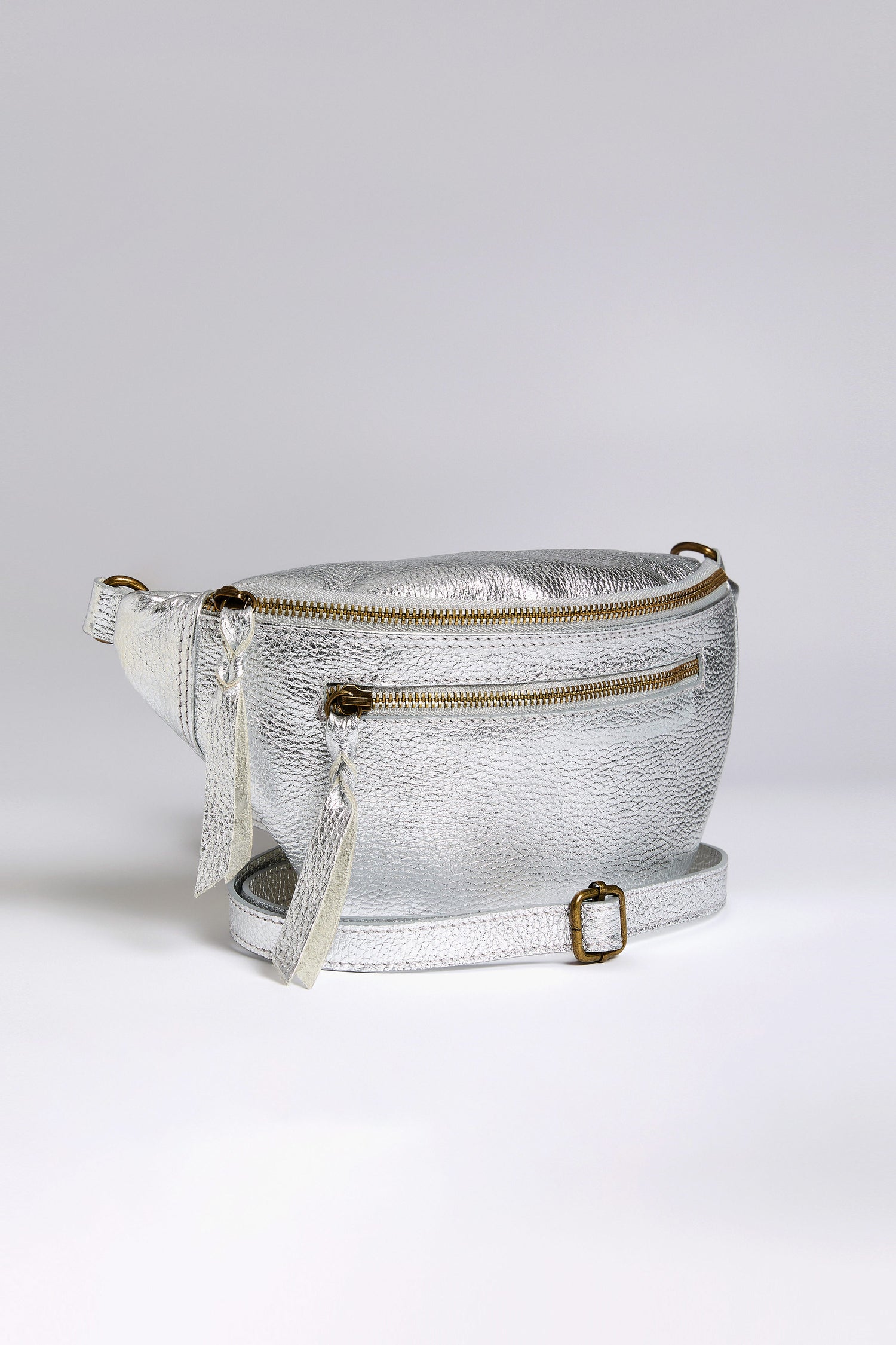 The Metallic Leather Crossbody Bag by Doris Maroquinerie showcases a main zip compartment, a front zip pocket, and tassel accents. Crafted from iridescent leather, it features an adjustable buckle strap for versatile wear.