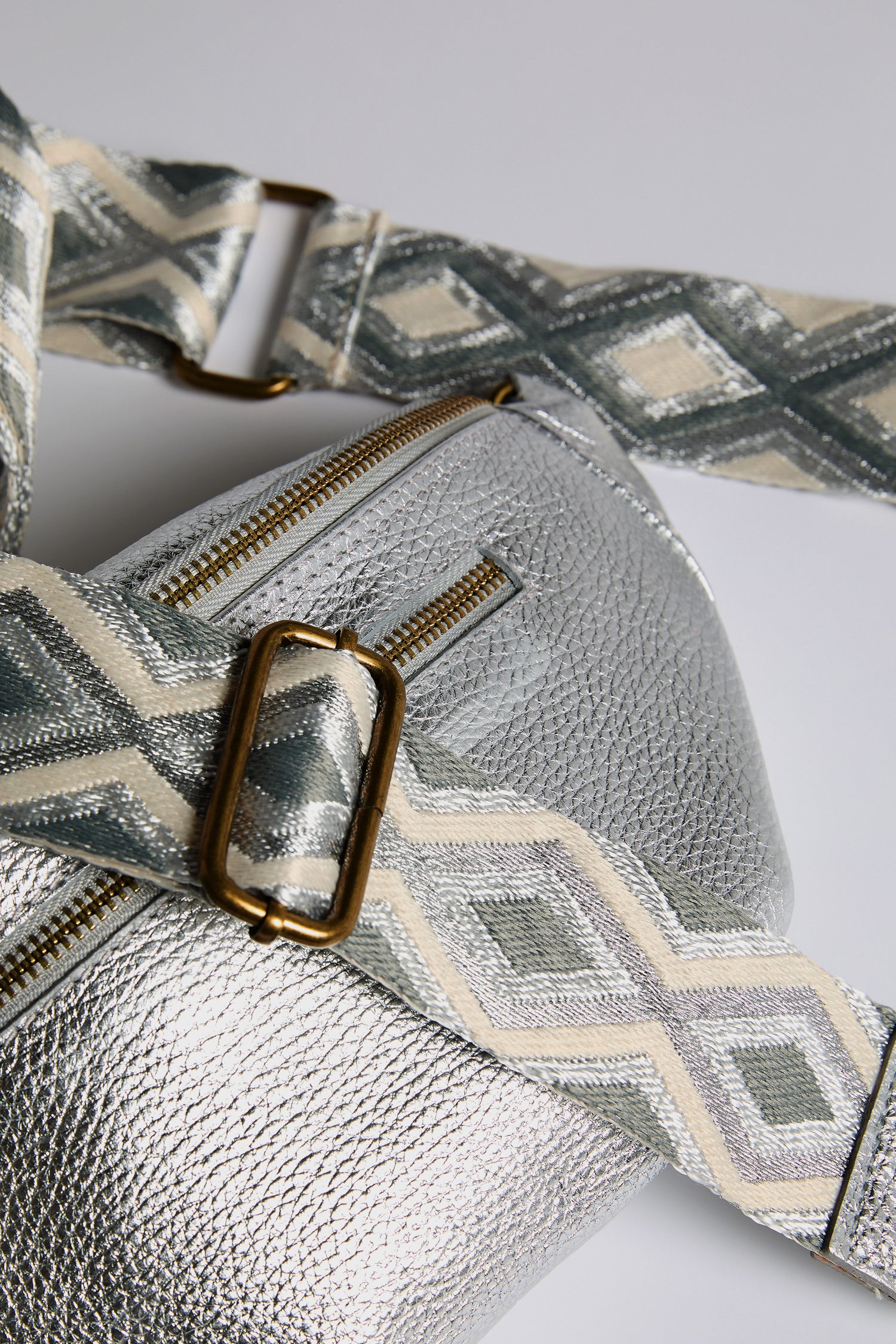 Close-up of a Doris Maroquinerie Metallic Leather Crossbody Bag with a geometric patterned strap in grey, beige, and white, highlighted by gold-tone hardware.