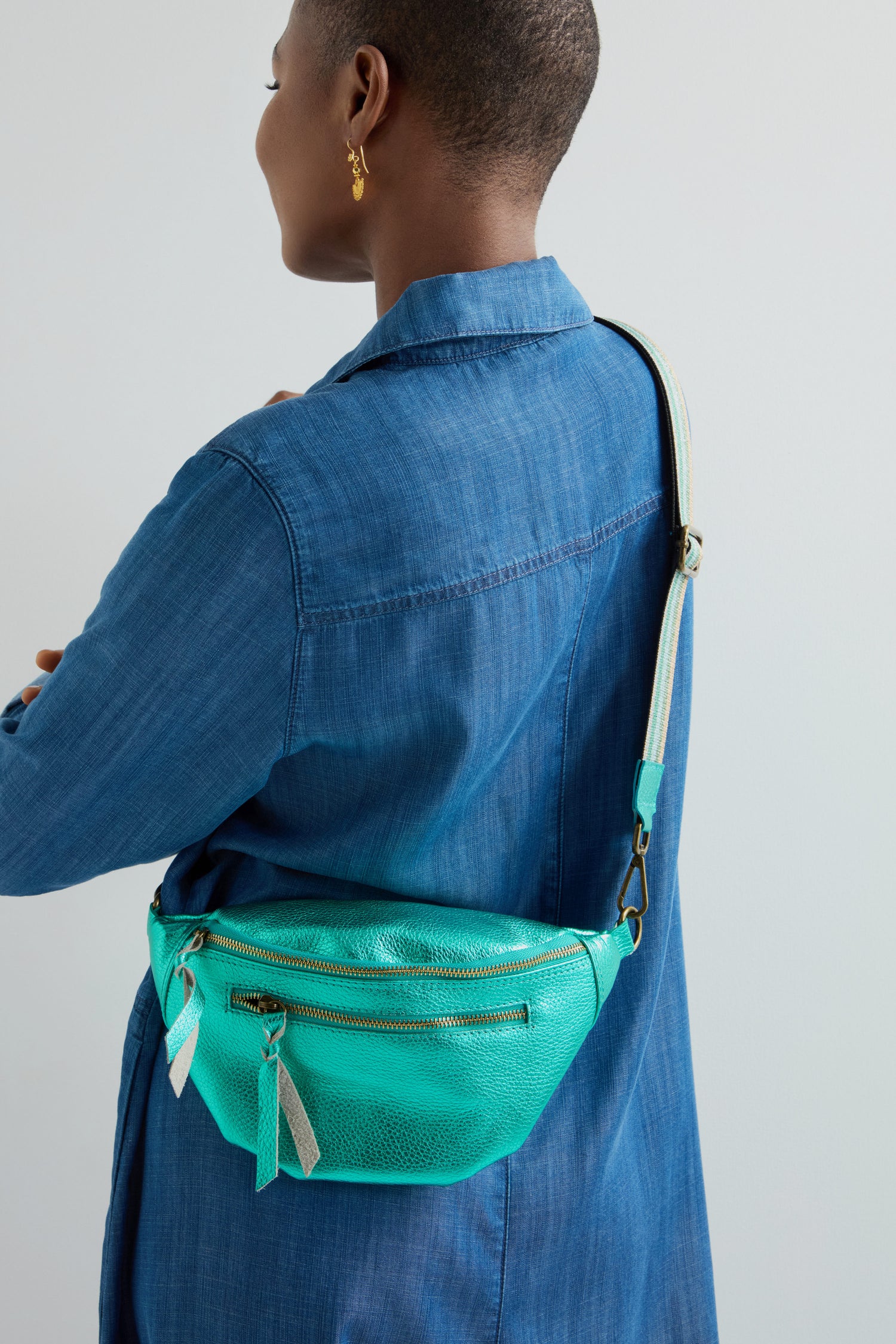 A person in a blue denim shirt carries a striking Metallic Leather Crossbody Bag by Doris Maroquinerie, featuring an eye-catching design with multiple zippers for both style and function.
