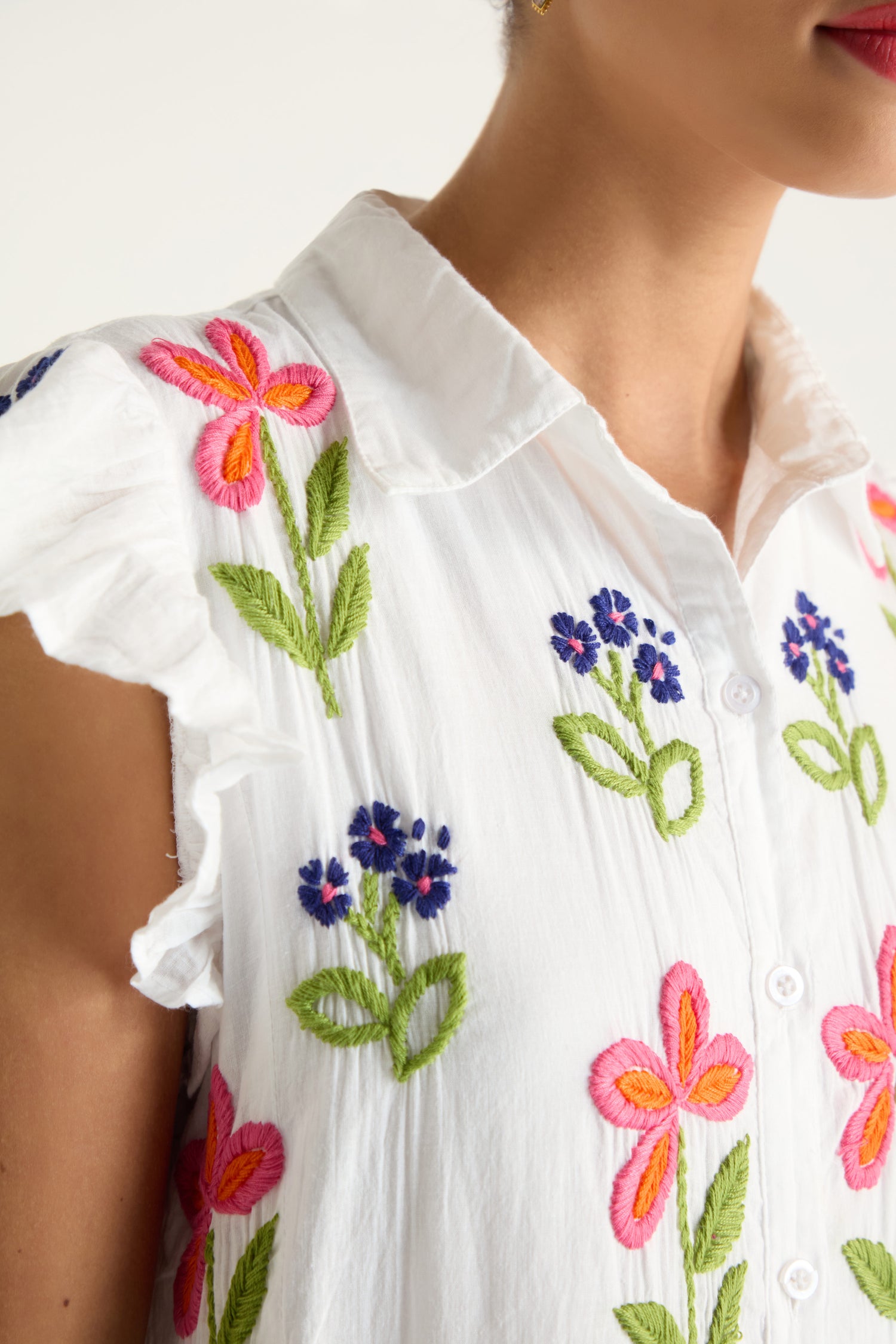 A close-up of a person wearing the Embroidered Flower Frill Sleeve Dress, featuring a white collar, colorful floral embroidery, and ruffled sleeves.