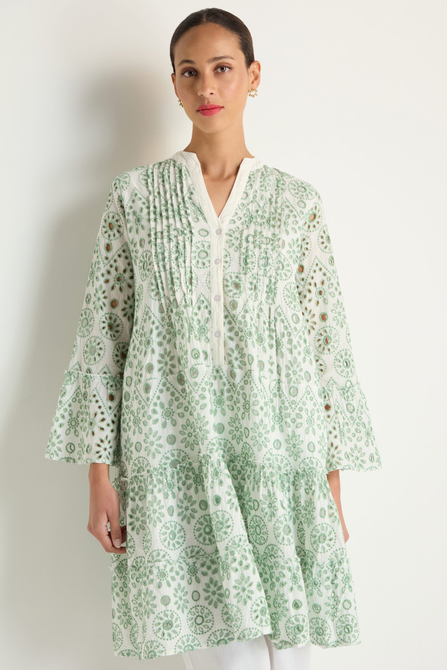 A woman models the Embroidered Circle Flared Sleeve Tunic in light green and white, featuring pleated details, white buttons, and Broderie anglaise embroidery, standing against a plain background.