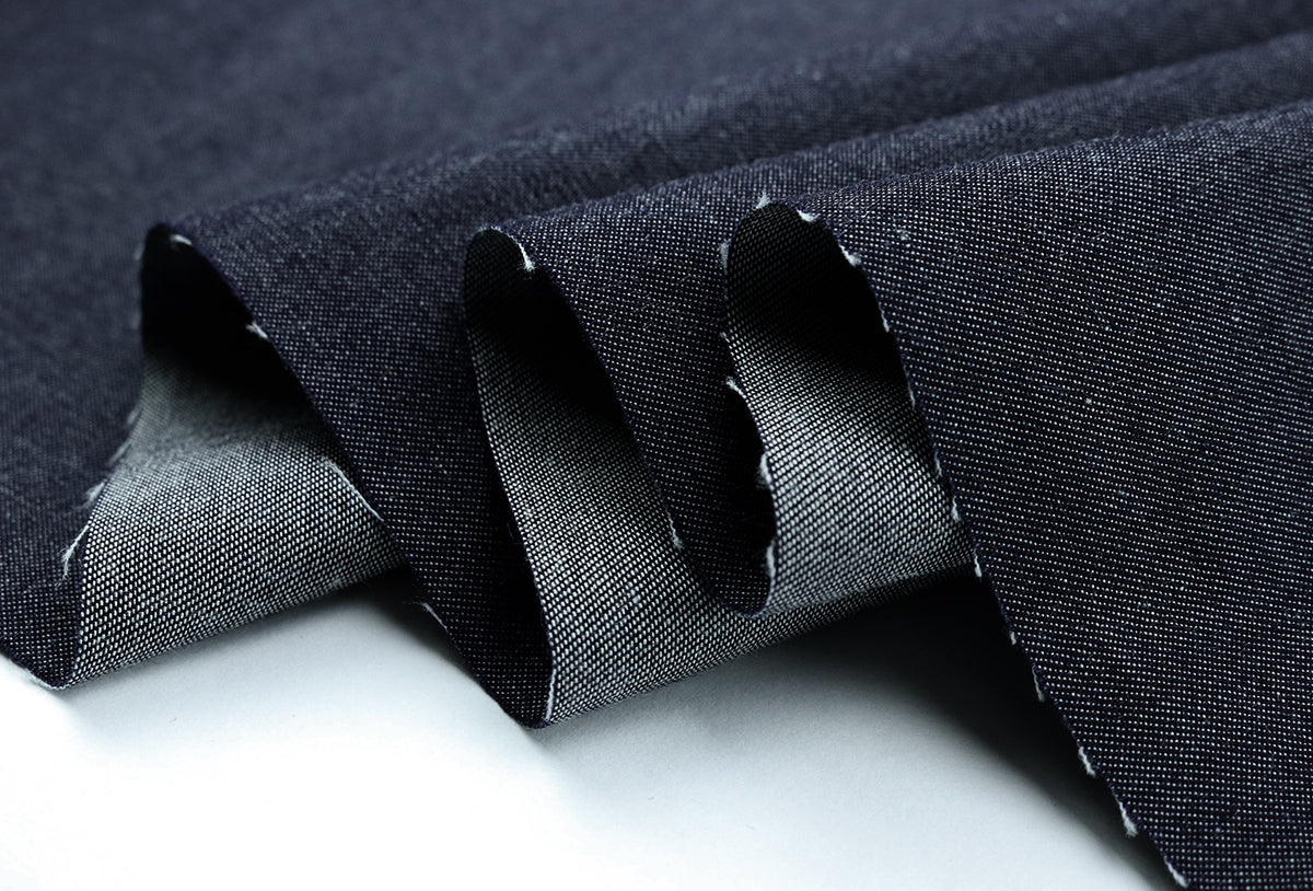 A image of a dark denim fabric folded back to reveal a lighter, textured underside, creating soft waves.