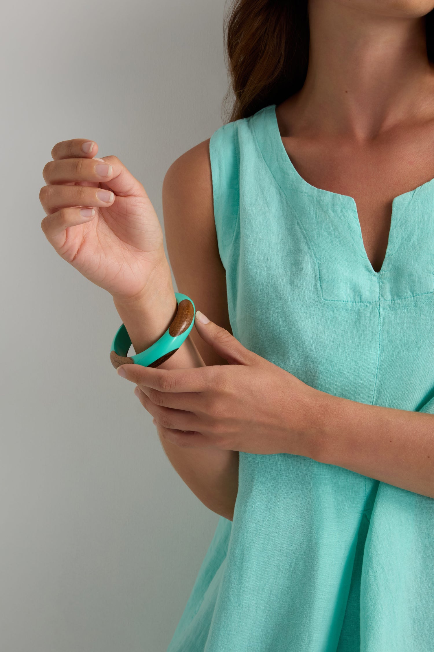 A woman in a sleeveless light turquoise top showcases her wrist, adorned with the Dotty Turquoise Wooden Bangle—a bold accessory featuring turquoise and wooden inlays.