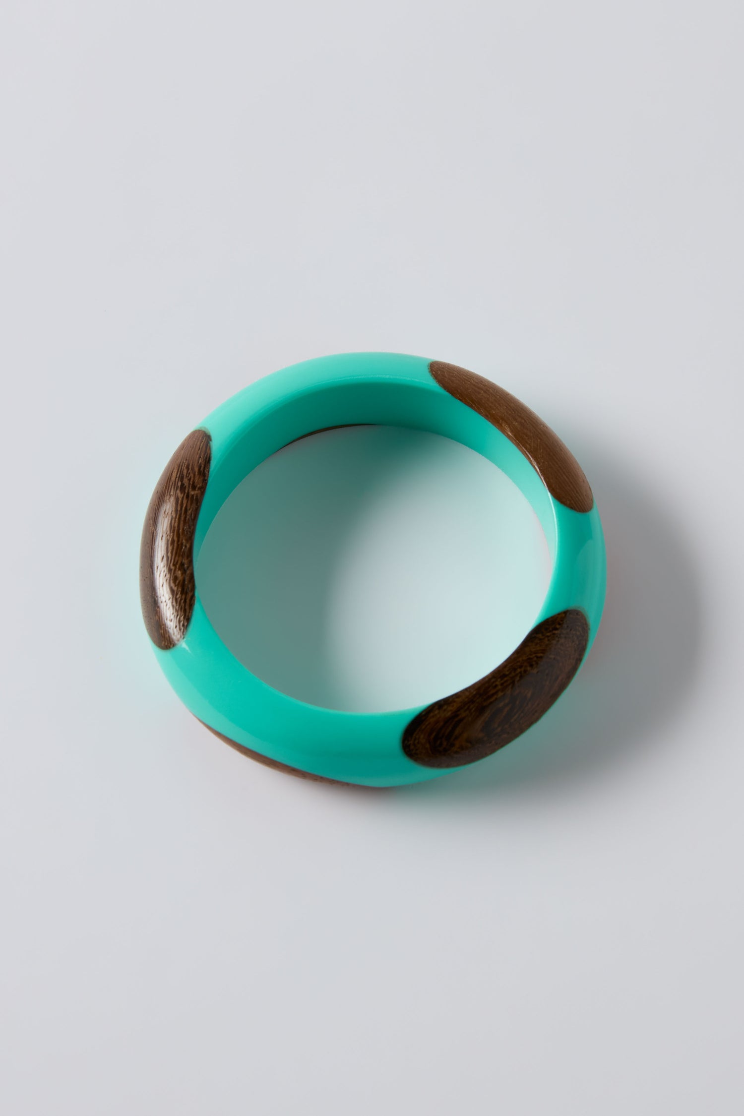 The Dotty Turquoise Wooden Bangle, featuring three oval wooden inlays, stands out against a plain light gray background—an eye-catching statement piece for any accessory collection.