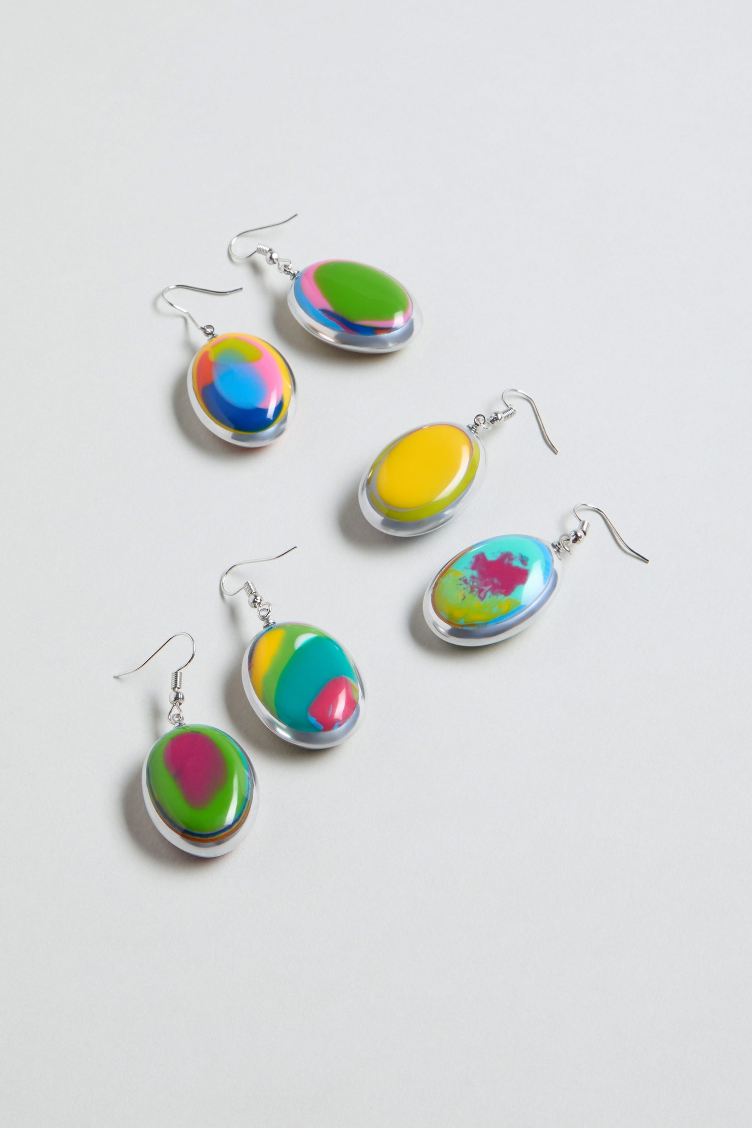 Five pairs of Rainbow Pebble Earrings with silver hooks, each displaying a colorful abstract swirl in green, yellow, pink, blue, and orange tones, are arranged on a white background.