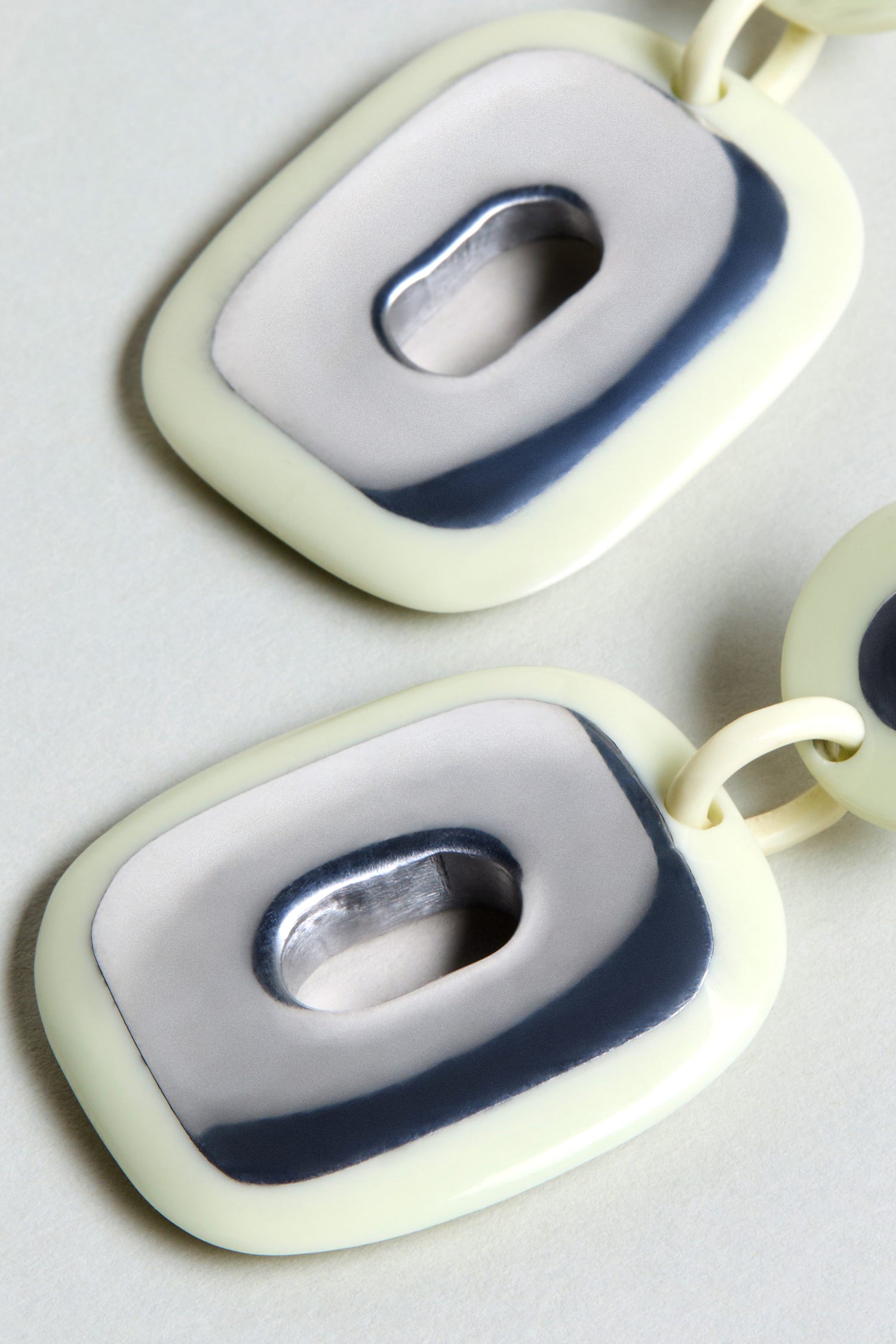 Close-up of two connected cream and gray rectangular links with oval openings and glossy finish—ideal as bold statement Deco Earrings.