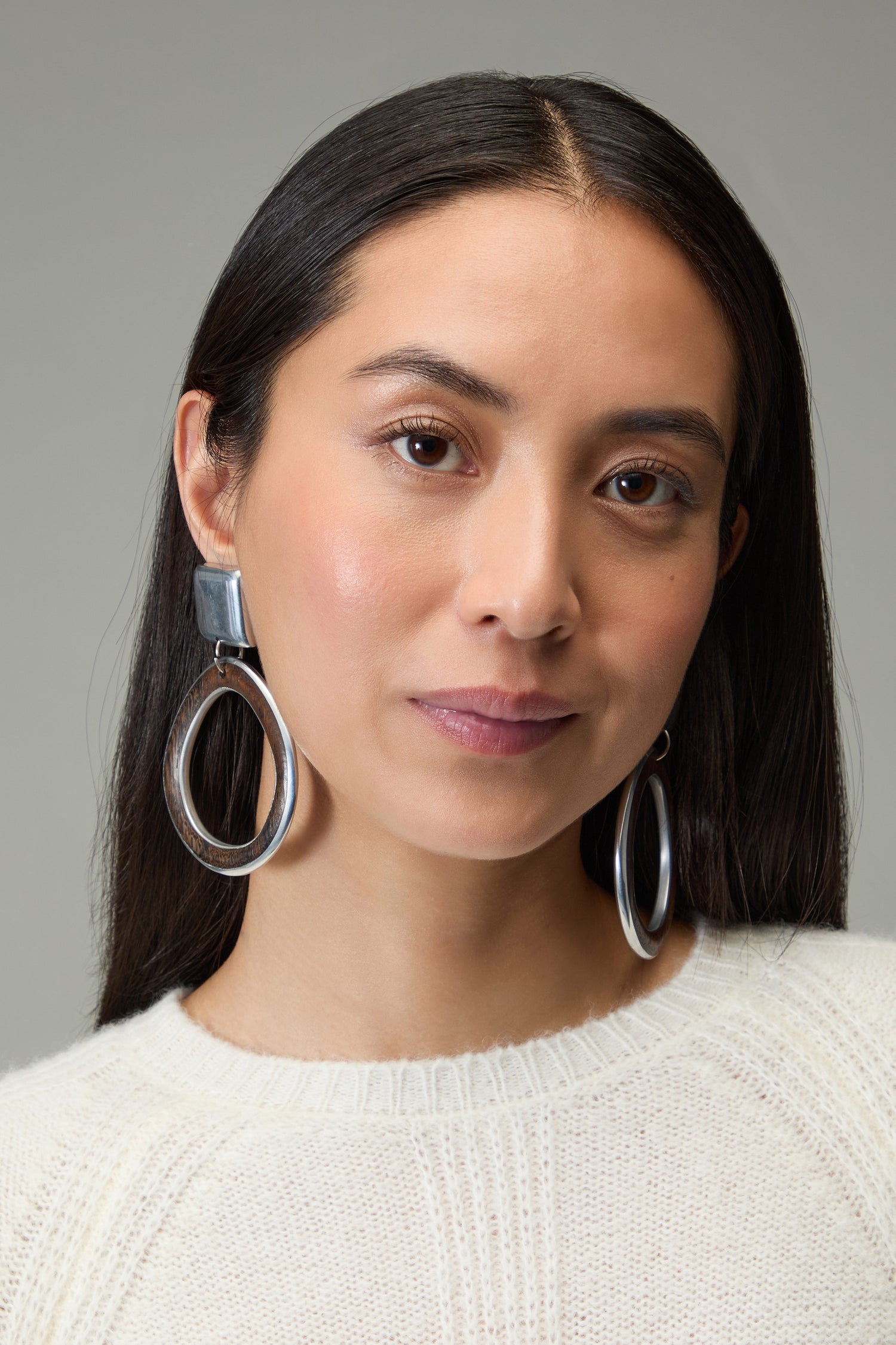 A woman with long dark hair in a white knit sweater wears Silver Squares Clip-On Earrings, looking at the camera with a neutral expression against a plain background.