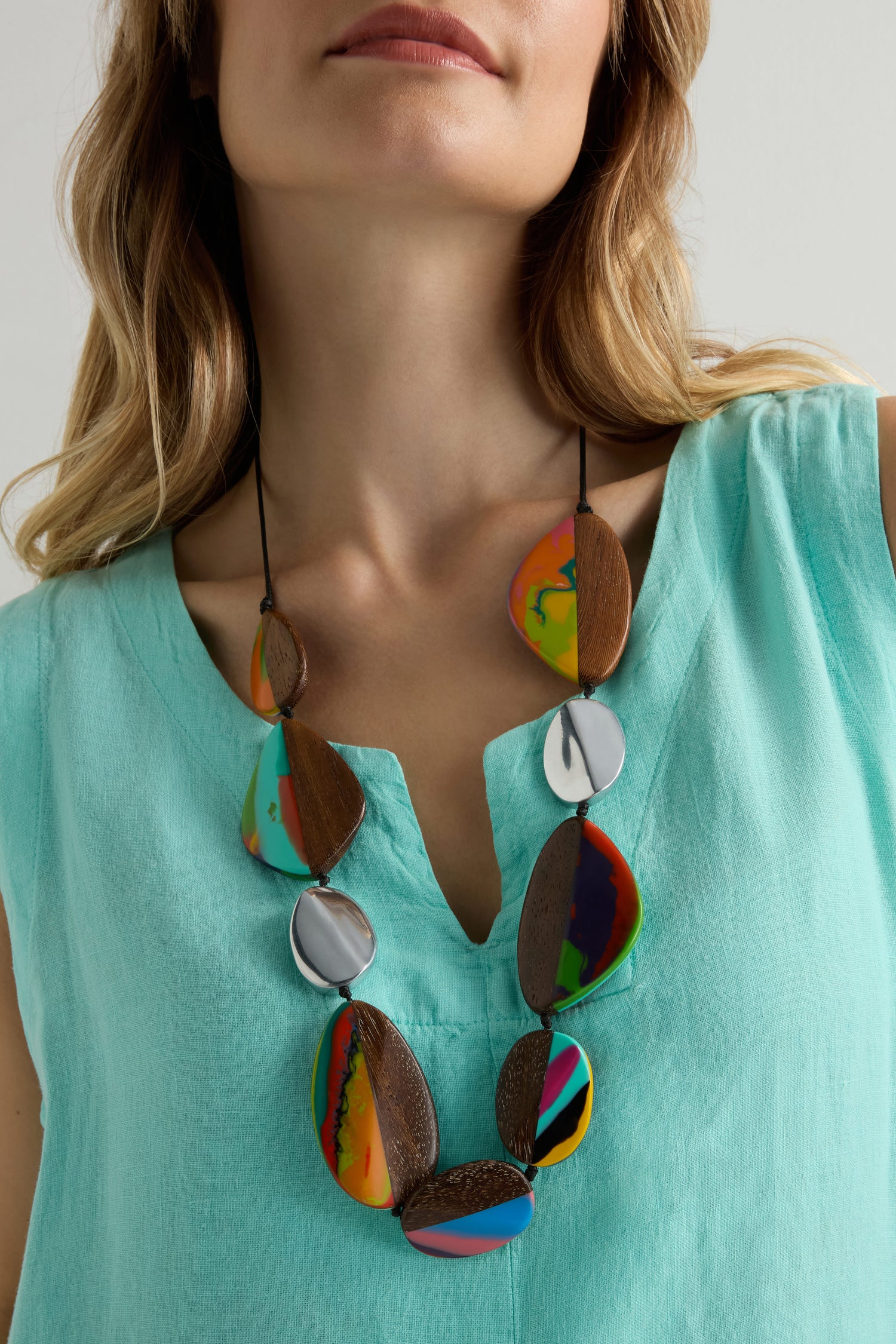 A woman wears a sleeveless aqua blouse and a colorful Marble Resin Pebble Necklace featuring large oval beads with marbled resin textures.
