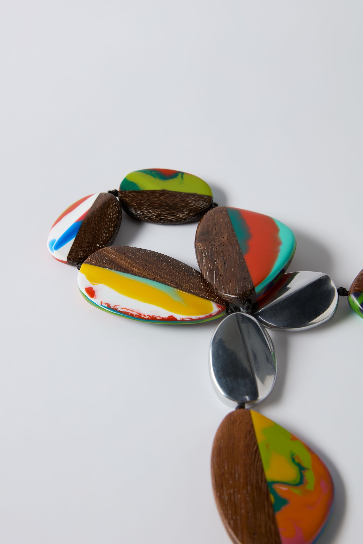 The Marble Resin Pebble Necklace by Ernesto de Barcelona features large oval beads of marbled resin, wood, and shiny metal segments, displayed on a white surface.