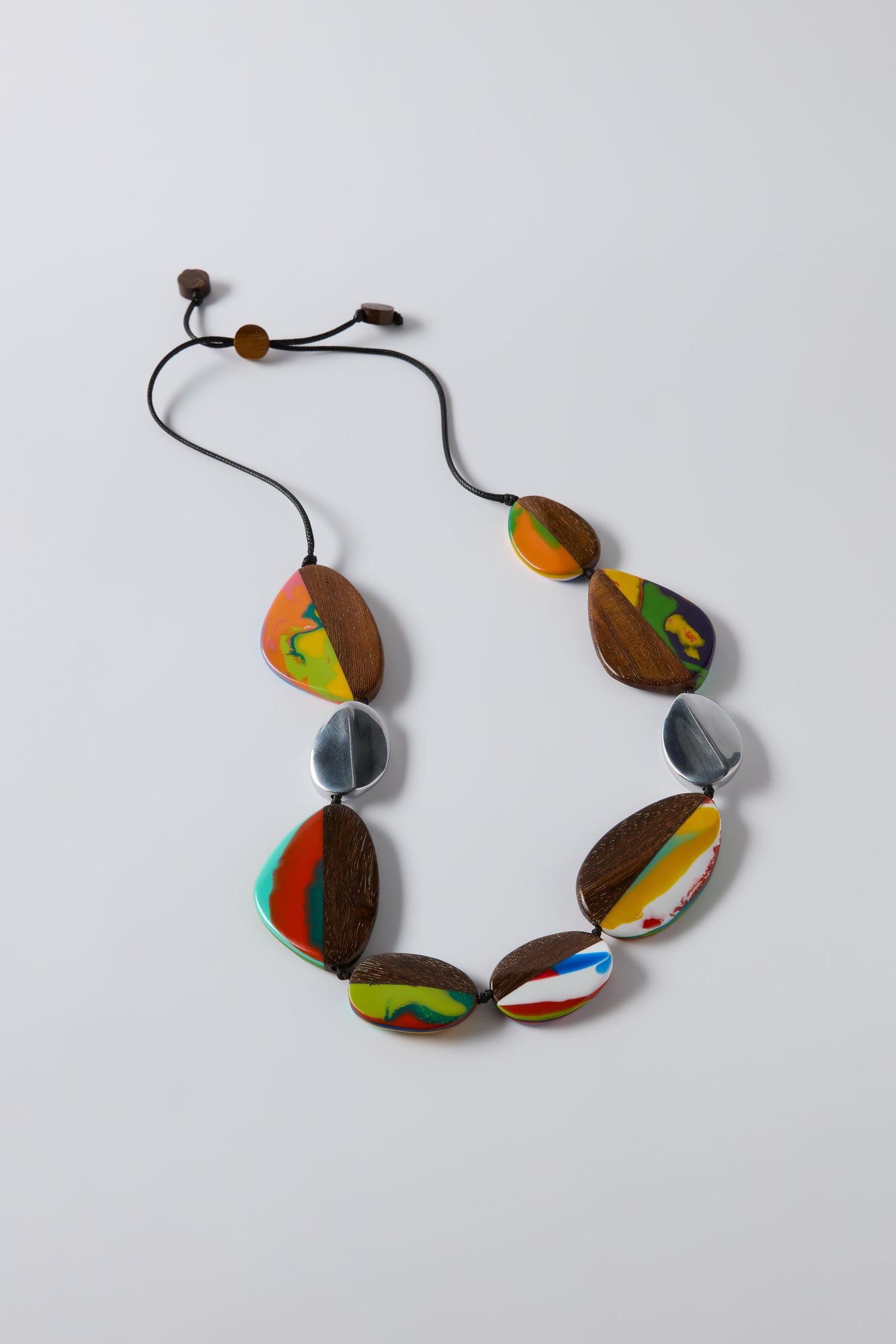 The Marble Resin Pebble Necklace by Ernesto de Barcelona features irregular wood, silver, and colorful marbled resin beads on a black adjustable cord, shown against a white background.