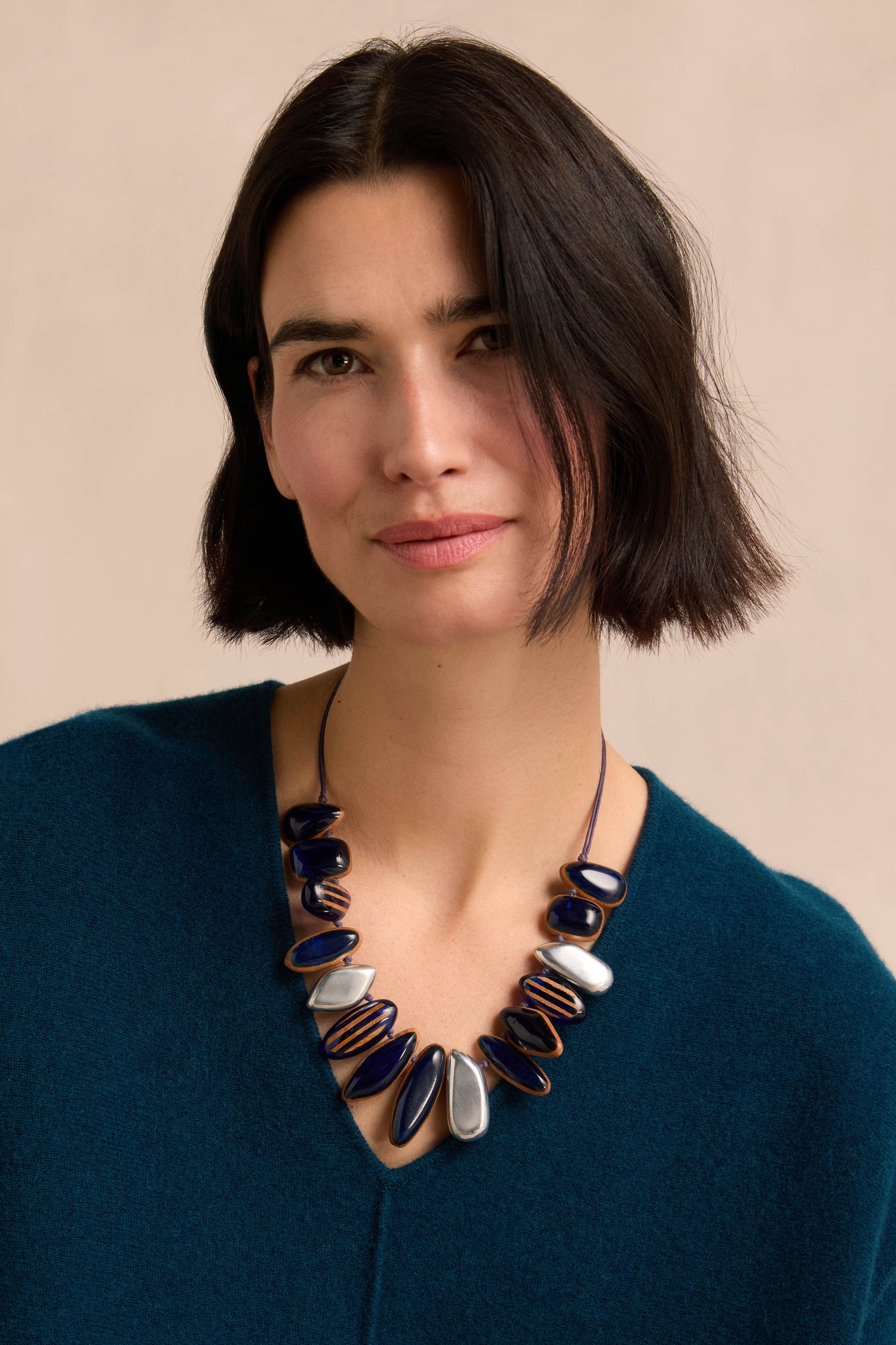 A woman with short dark hair wears a teal sweater and the Resin Pebble Necklace, posing against a plain light background.