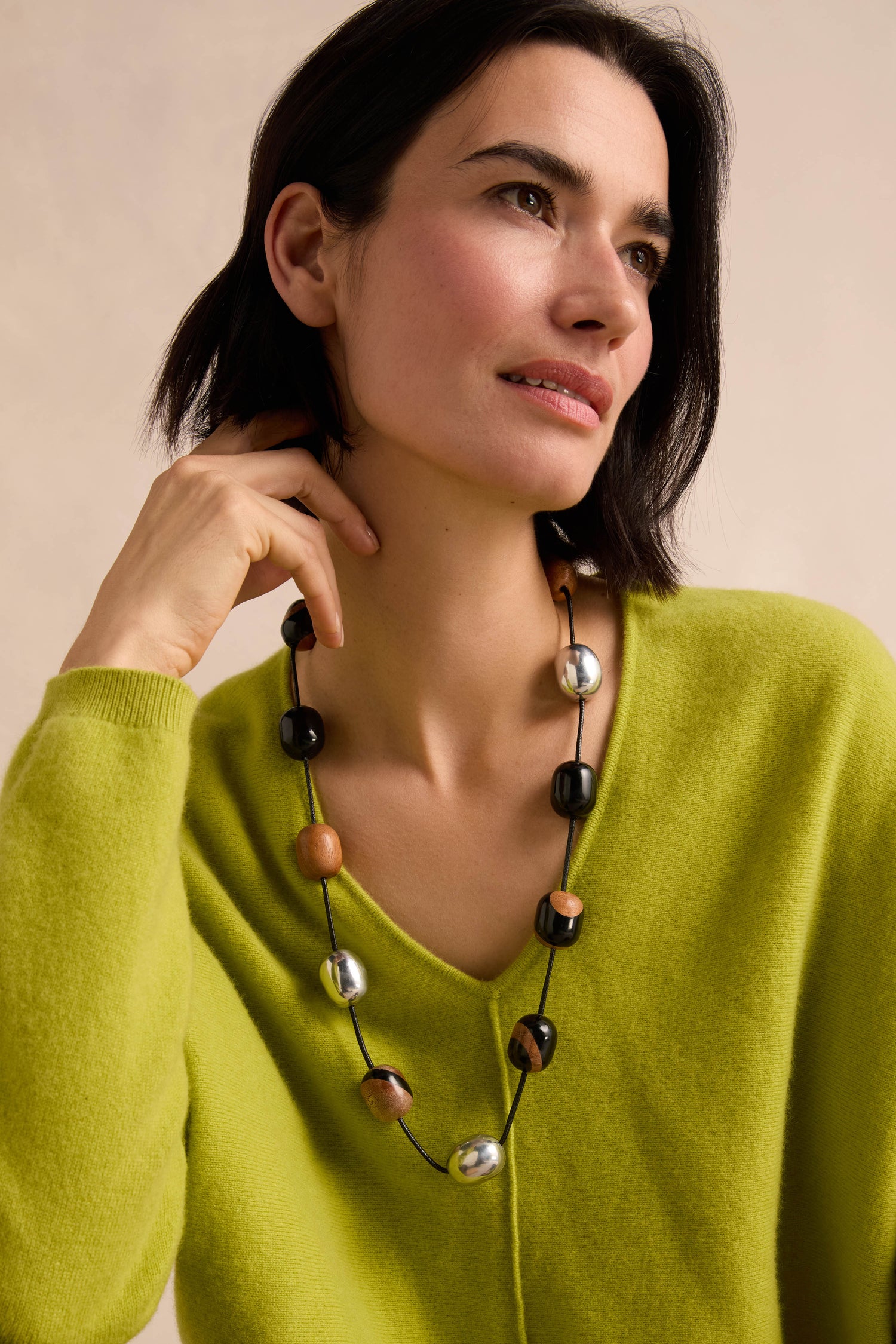 Woman wearing a lime green sweater and the Long Allsorts Necklace—a long resin necklace with black, silver, and brown beads—looking off to the side with a neutral expression.