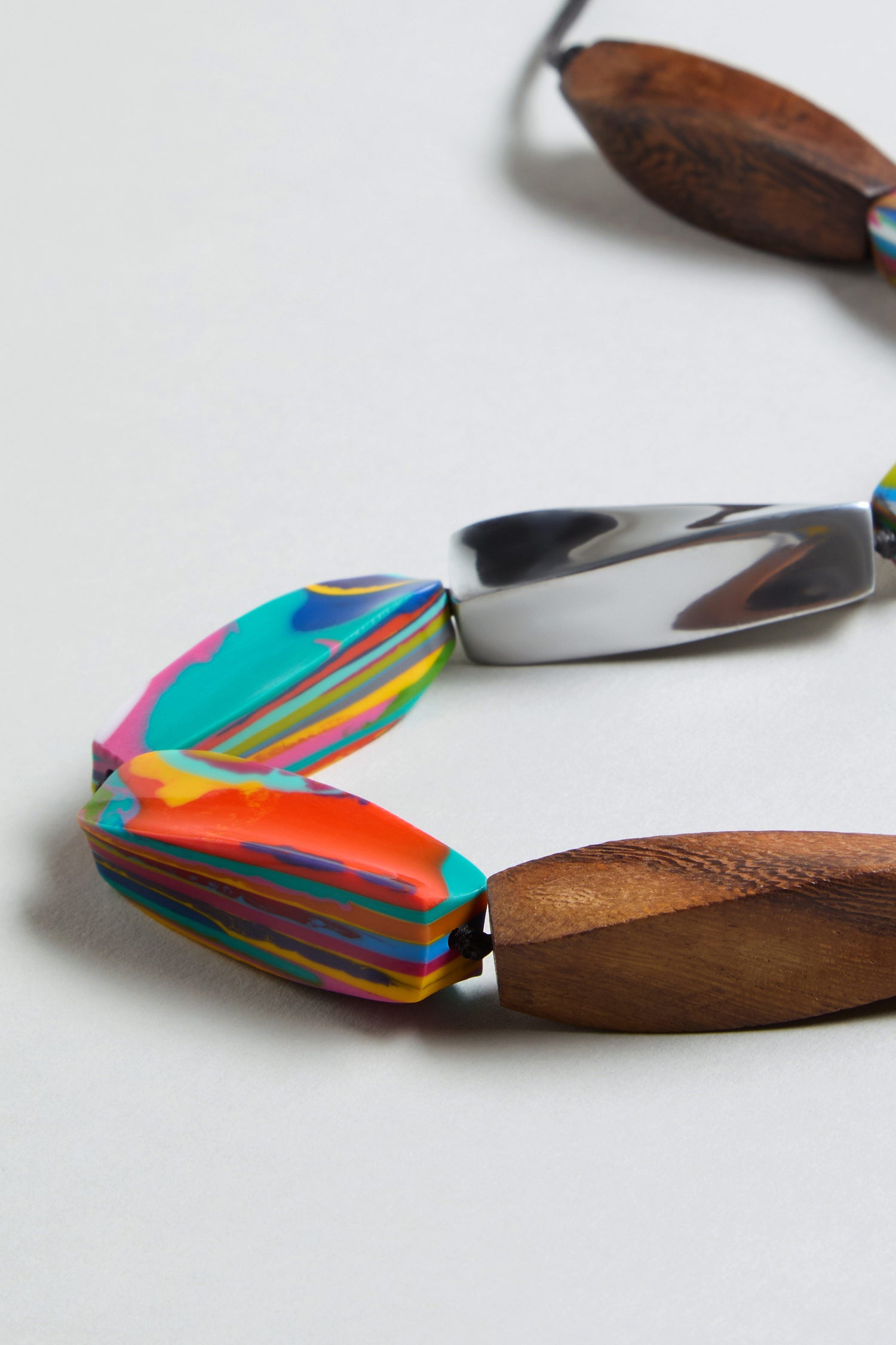 Close-up of the Twisted Shapes Necklace with multicolored marbled beads, carved wooden beads, and recycled aluminum accents shown on a light background.