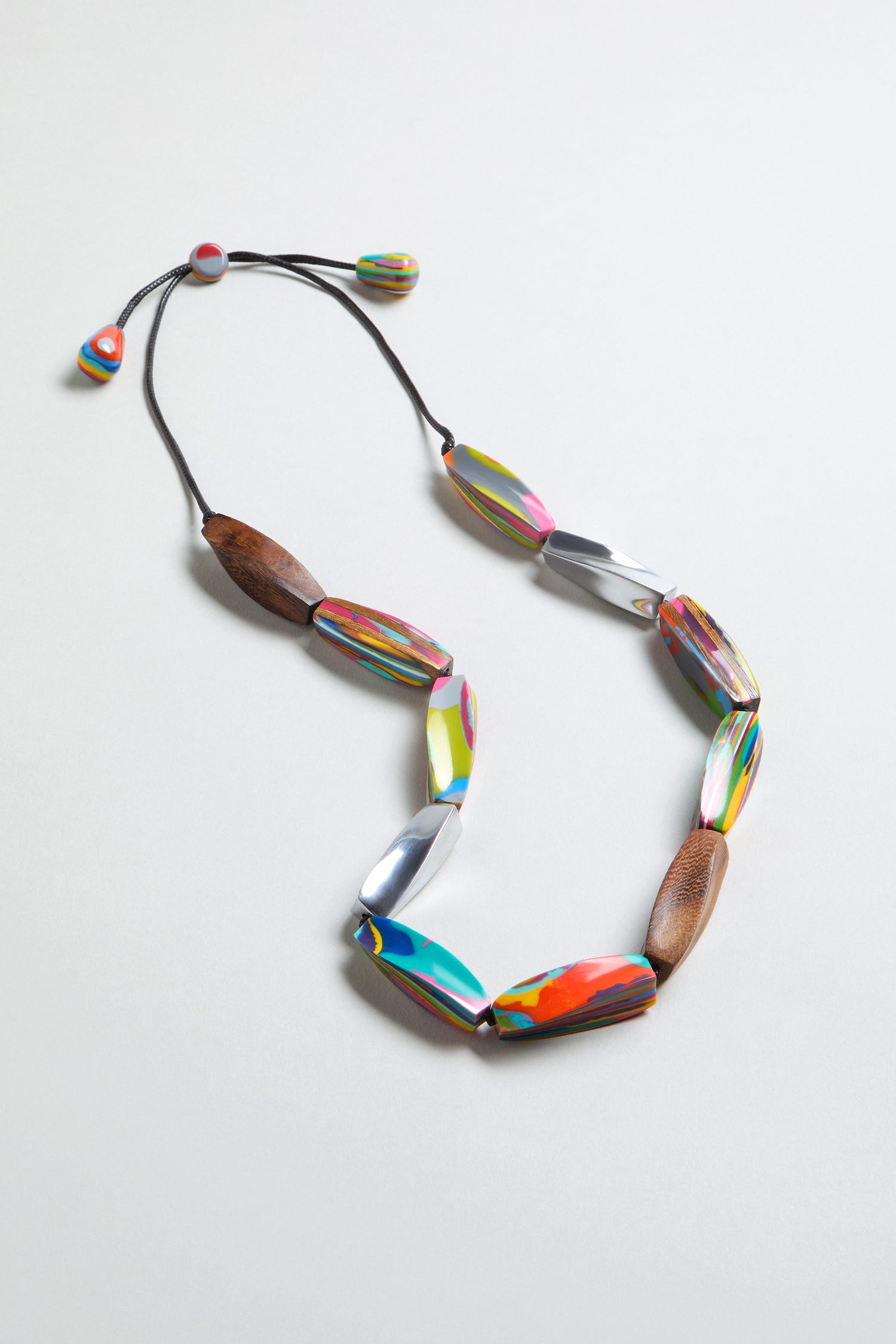 The Twisted Shapes Necklace showcases colorful oval beads and natural wood accents, set against a white background.