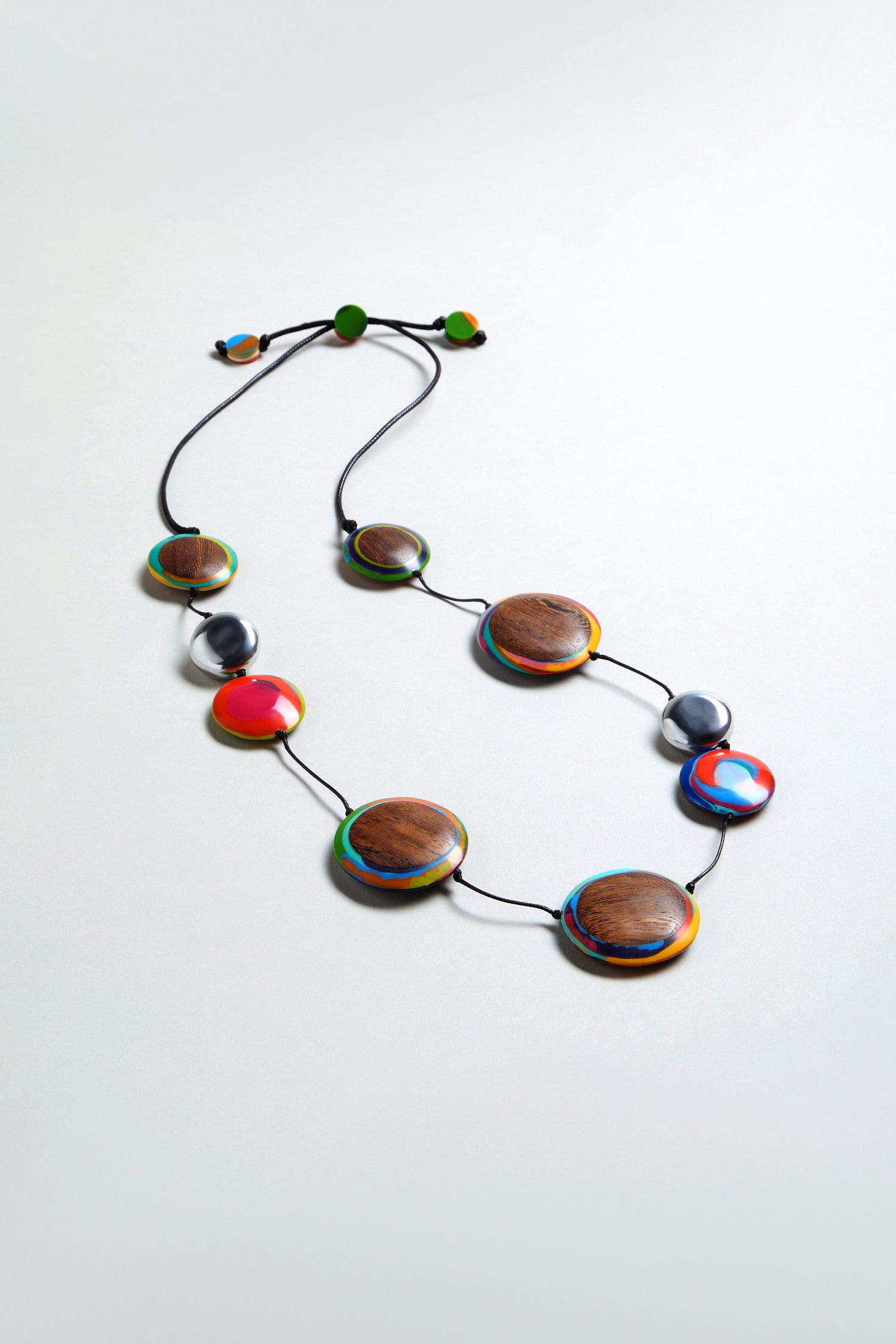 The Planetary Necklace features large round wood and multicolour resin beads on a black cord, displayed against a light gray background.