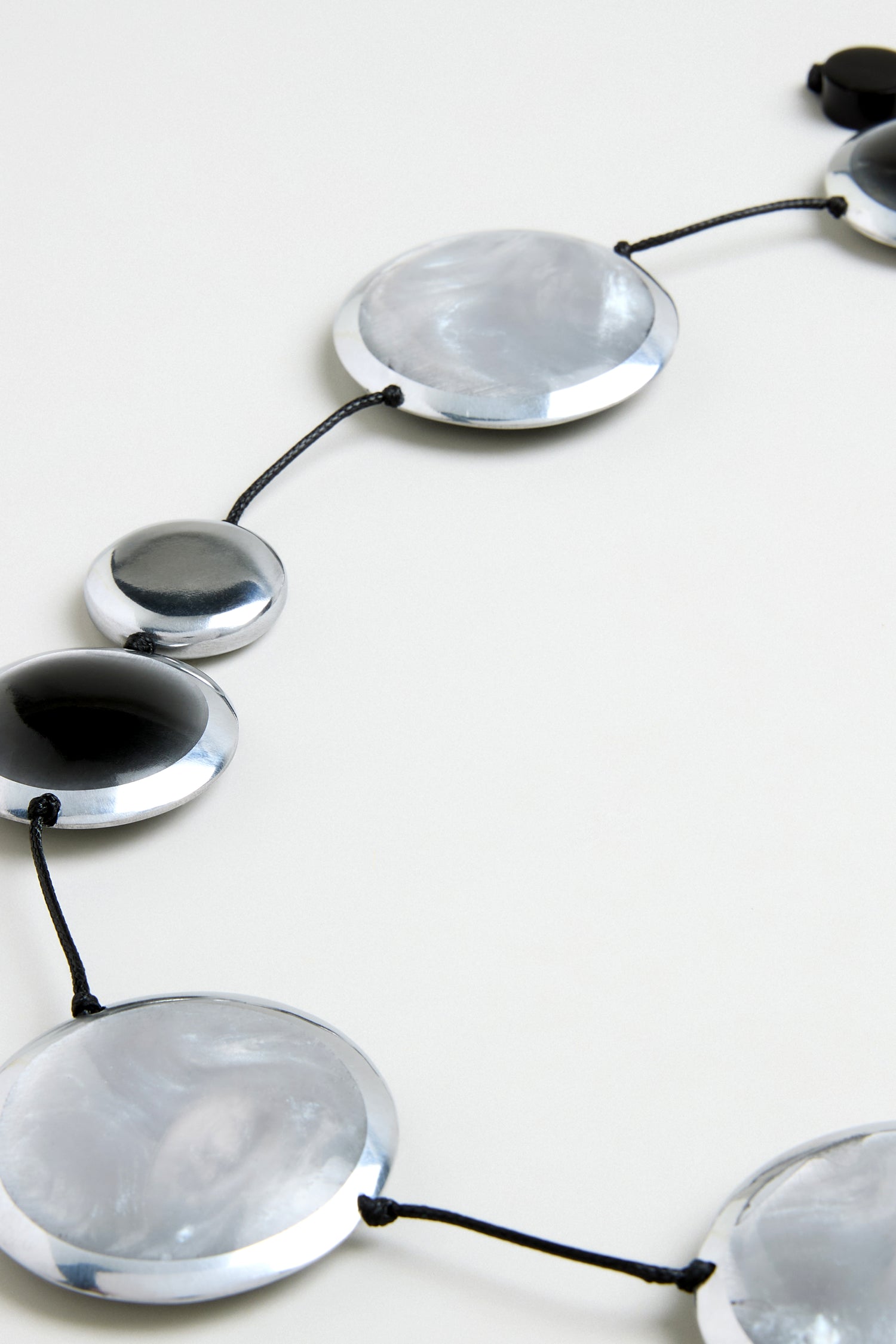 The Orbit Necklace features large round silver and black beads on a black cord, showcasing modern design. It is elegantly displayed on a light surface.