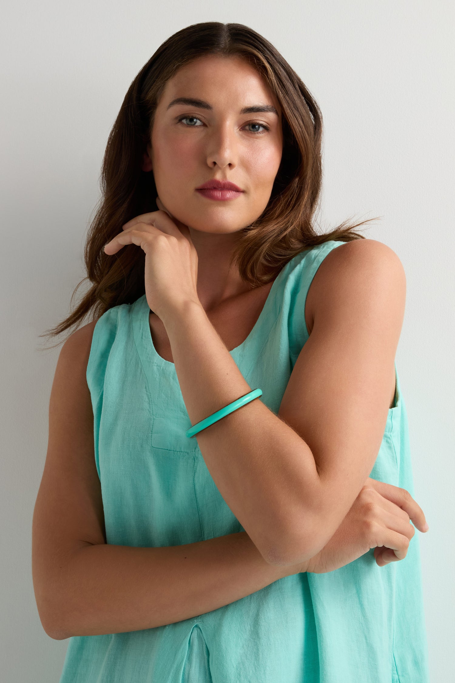 A woman with long brown hair wears a sleeveless light turquoise top and the Cosmos Turquoise Wooden Bangle, the perfect summer accessory, standing against a plain white background.